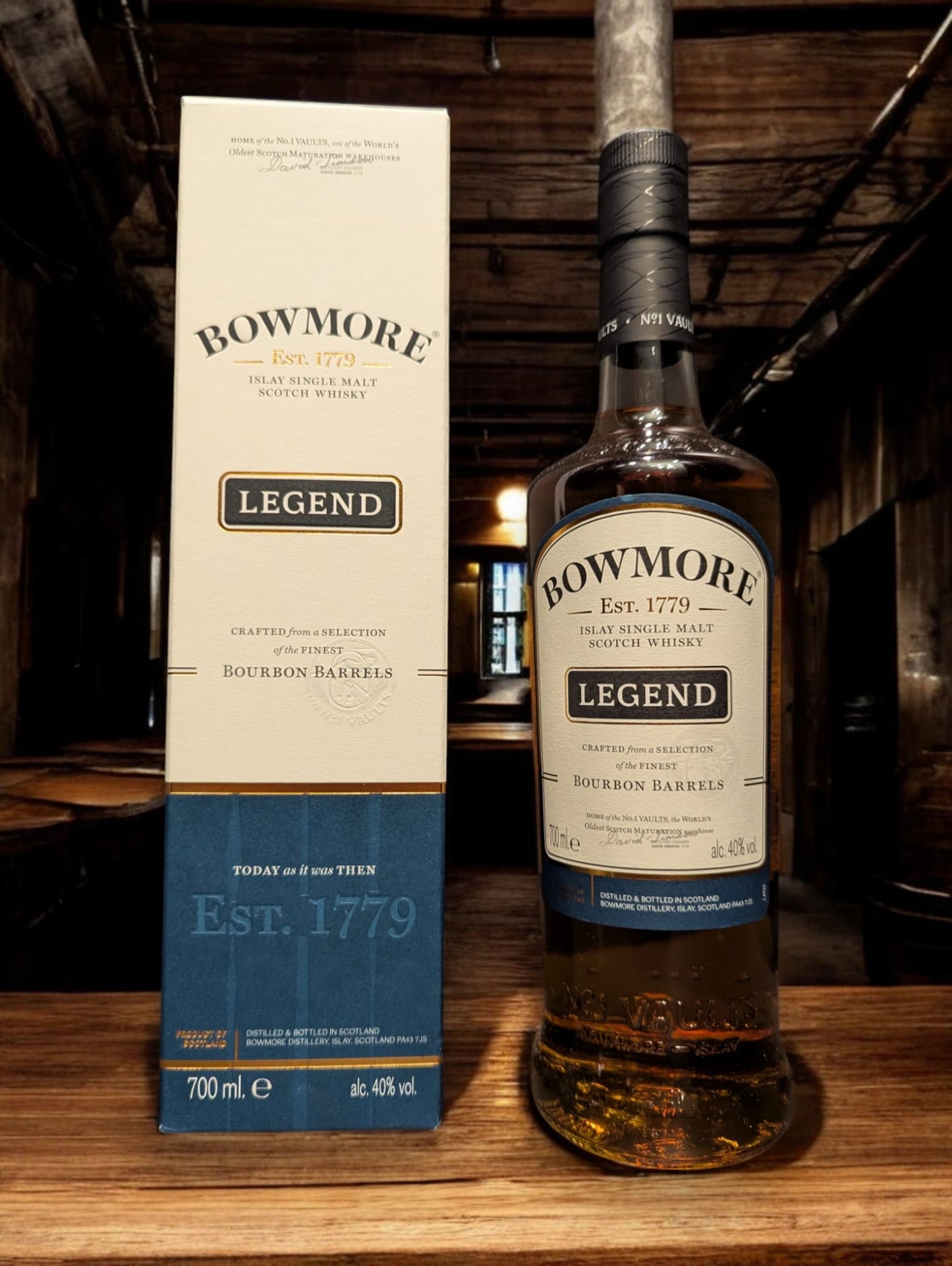 Eine Flasche Bowmore Legend Whisky in einer klassischen Destilleriehalle, umgeben von Holzbalken, Steinwänden und Whiskyfässern. Die schlichte, elegante Flasche mit ihrem charakteristischen Etikett fügt sich harmonisch in die traditionelle, maritime Atmosphäre der Bowmore-Destillerie ein.