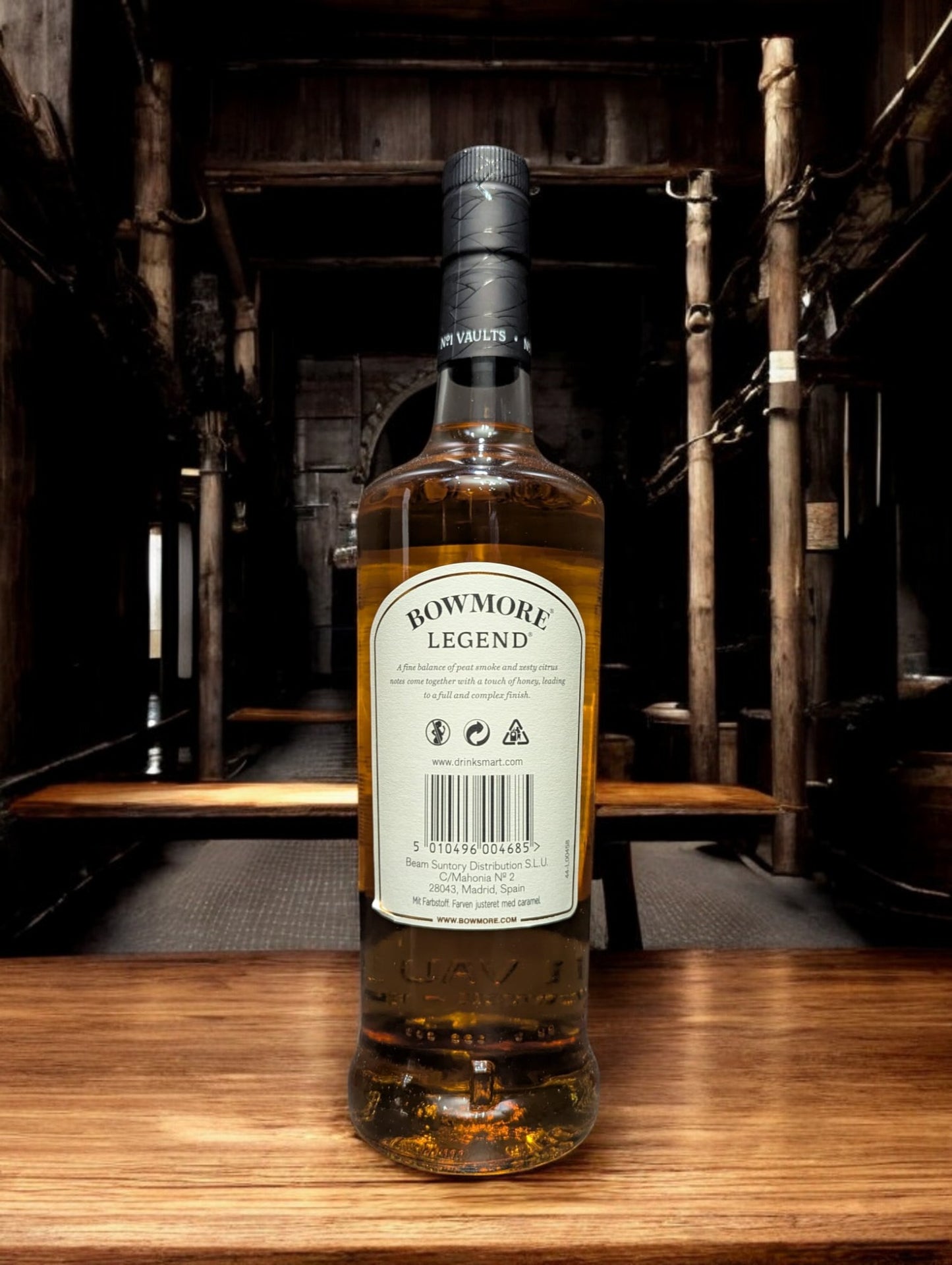 Eine Flasche Bowmore Legend Whisky in einer klassischen Destilleriehalle, umgeben von Holzbalken, Steinwänden und Whiskyfässern. Die schlichte, elegante Flasche mit ihrem charakteristischen Etikett fügt sich harmonisch in die traditionelle, maritime Atmosphäre der Bowmore-Destillerie ein.