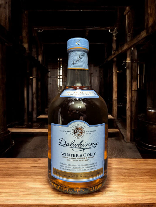 Eine Flasche Dalwhinnie Winter's Gold Whisky in einer malerischen Destilleriehalle, umgeben von Steinwänden und Holzbalken, mit einem Hauch von frostiger Kälte in der Luft. Die honigfarbene Flasche mit ihrem winterlichen Etikett vermittelt Wärme und Eleganz, während die rustikale Umgebung die Verbindung zur schottischen Berglandschaft und den eisigen Temperaturen, bei denen dieser Whisky reift, betont.