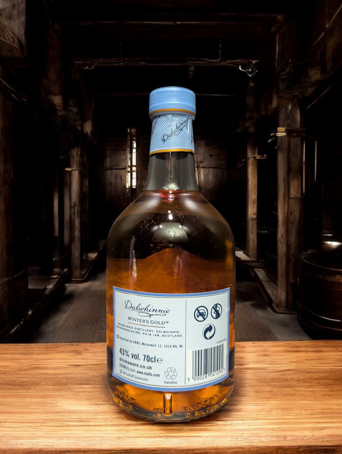 Eine Flasche Dalwhinnie Winter's Gold Whisky in einer malerischen Destilleriehalle, umgeben von Steinwänden und Holzbalken, mit einem Hauch von frostiger Kälte in der Luft. Die honigfarbene Flasche mit ihrem winterlichen Etikett vermittelt Wärme und Eleganz, während die rustikale Umgebung die Verbindung zur schottischen Berglandschaft und den eisigen Temperaturen, bei denen dieser Whisky reift, betont.