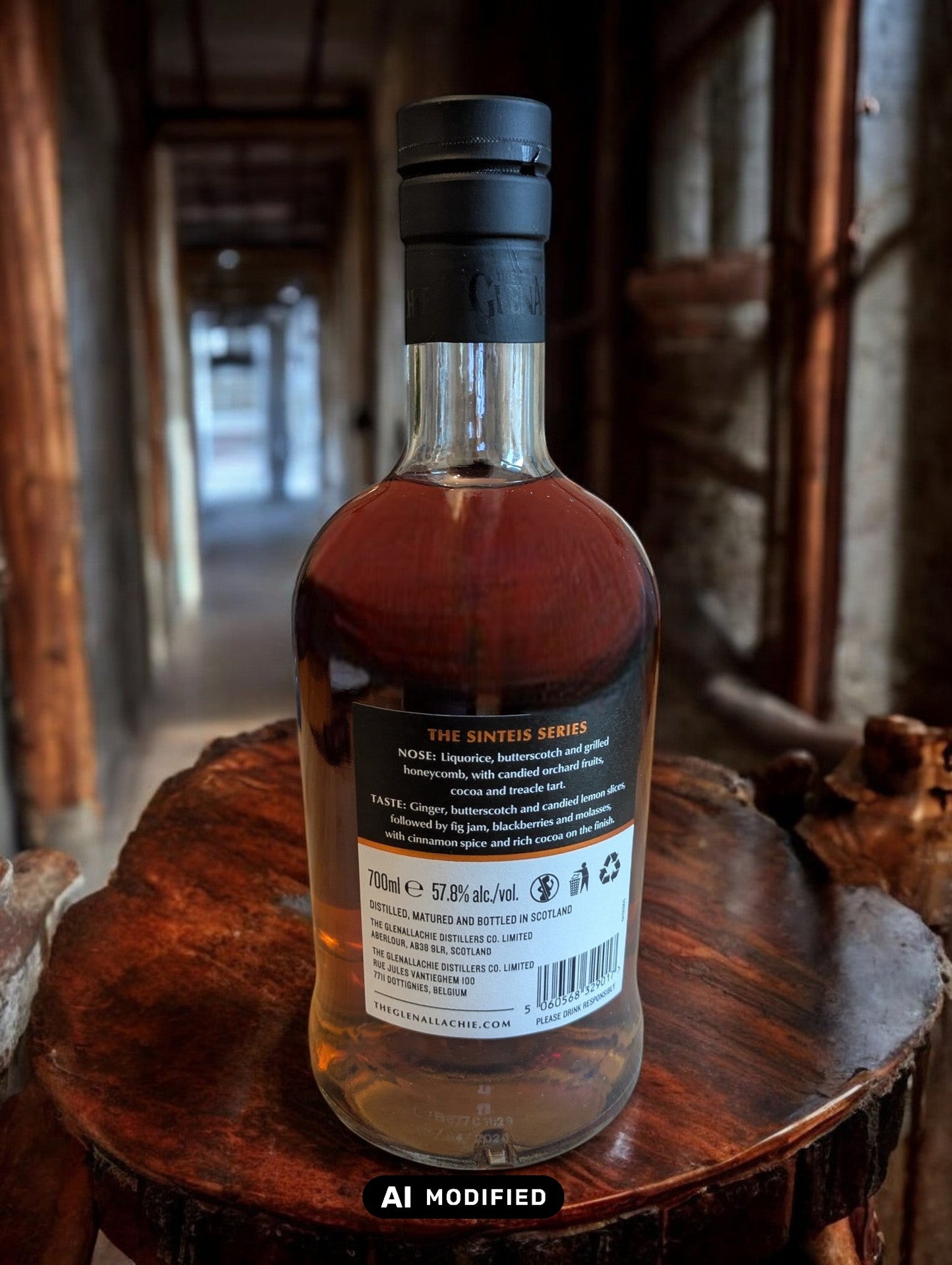 GlenAllachie Sinteis Part I Flasche auf einem niedrigen Holztisch, im Hintergrund eine dunkle Brennerei mit alten Holzfässern und kupfernen Brennblasen.