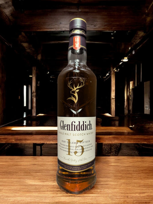 Ein Glenfiddich 15 Jahre Whisky in einer eleganten Flasche, umgeben von einer stilvollen Verpackung. Die goldene Farbe des Whiskys wird durch das Licht betont, während das Etikett die reiche Tradition und Qualität der Marke hervorhebt. Ideal präsentiert auf einem dunklen Holztisch mit einem passenden Whiskyglas, das einen Hauch von Luxus vermittelt.
