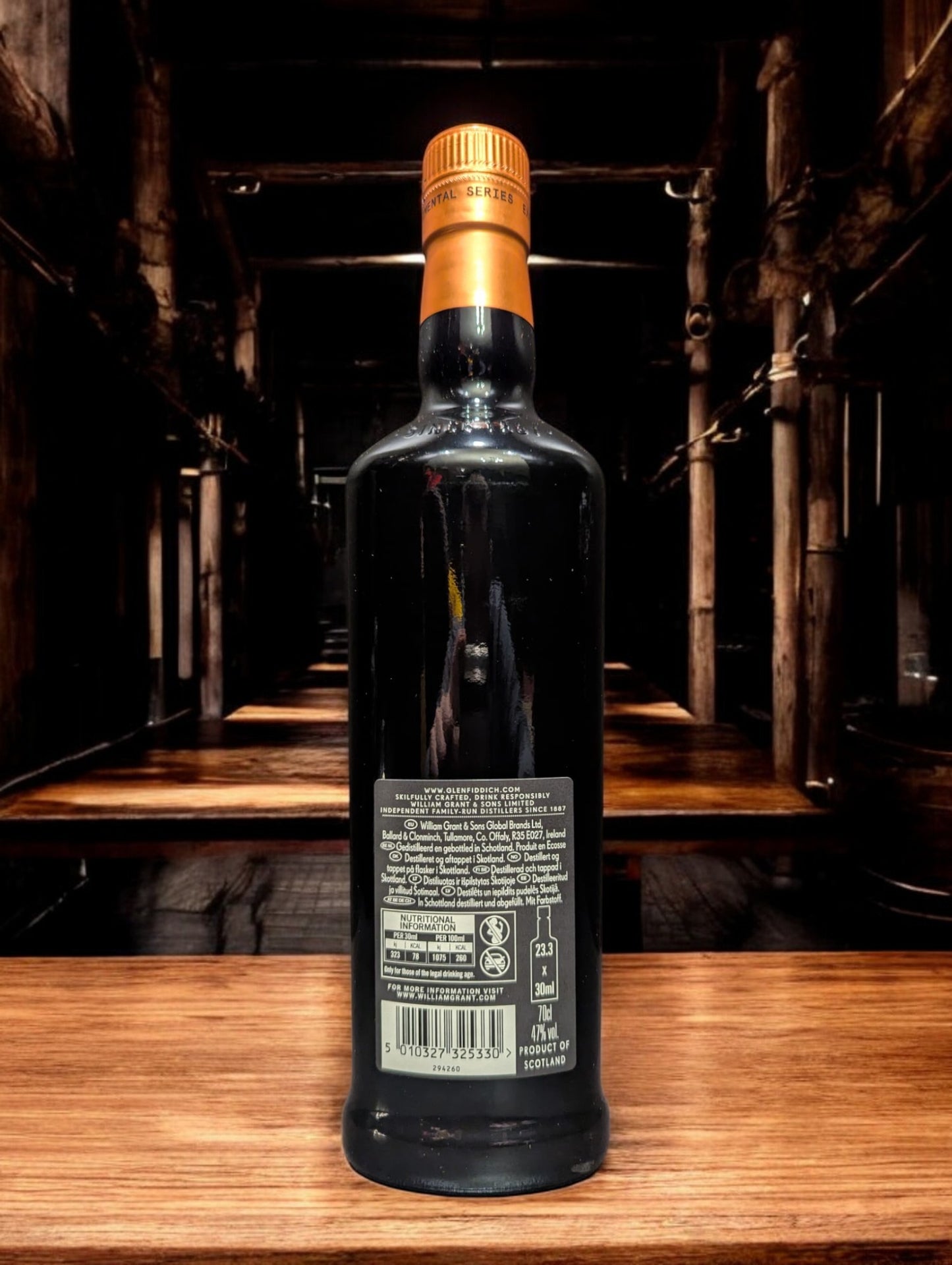 Ein elegantes Glenfiddich Project XX Whiskyfläschchen, präsentiert vor einem dunkelgrauen Hintergrund. Die Flasche besticht mit ihrem modernen Design: ein tiefschwarzes Etikett mit kupferfarbenem "XX"-Logo, das im Licht glänzt. Perfekt ausgeleuchtete Details betonen die hochwertige Verarbeitung, während der schlichte Hintergrund den Fokus auf das Produkt lenkt.