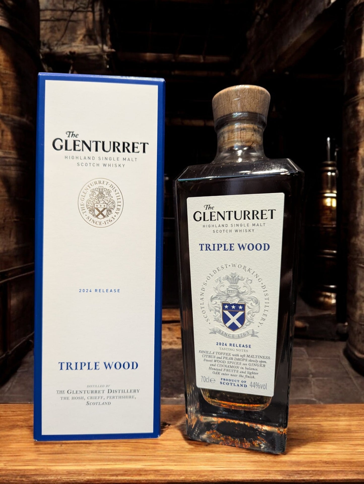 Glenturret Triple Wood Whiskyflasche elegant präsentiert mit sichtbaren Holzmaserungen im Hintergrund. Bernsteinfarbener Whisky reflektiert das Licht, während das Etikett die Reifung in drei verschiedenen Holzfässern hervorhebt. Dieses Bild betont die komplexe Handwerkskunst und die vielschichtigen Geschmacksnoten, die Liebhaber erwarten dürfen.