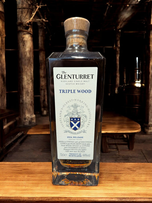 Glenturret Triple Wood Whiskyflasche elegant präsentiert mit sichtbaren Holzmaserungen im Hintergrund. Bernsteinfarbener Whisky reflektiert das Licht, während das Etikett die Reifung in drei verschiedenen Holzfässern hervorhebt. Dieses Bild betont die komplexe Handwerkskunst und die vielschichtigen Geschmacksnoten, die Liebhaber erwarten dürfen.