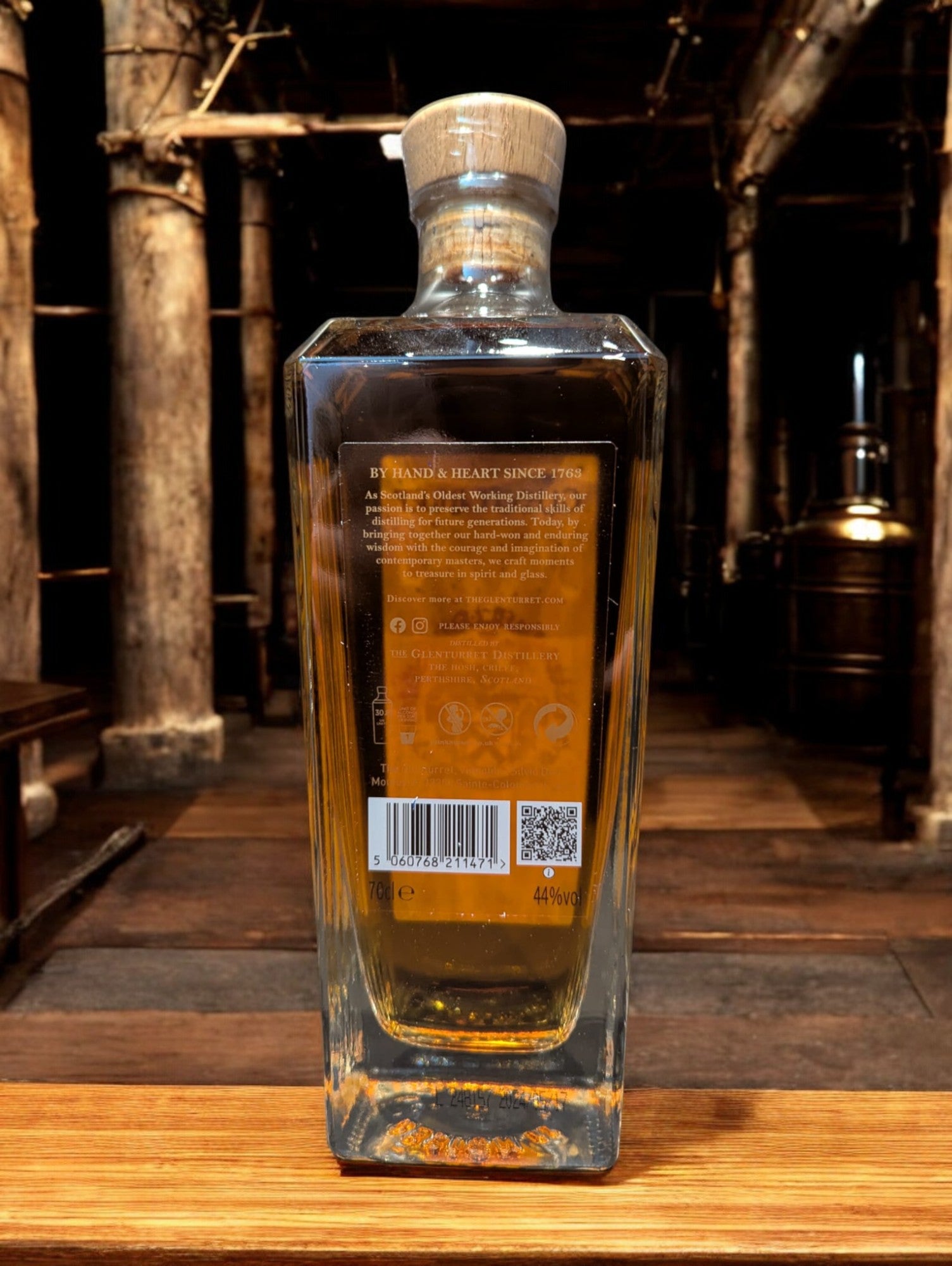 Glenturret Triple Wood Whiskyflasche elegant präsentiert mit sichtbaren Holzmaserungen im Hintergrund. Bernsteinfarbener Whisky reflektiert das Licht, während das Etikett die Reifung in drei verschiedenen Holzfässern hervorhebt. Dieses Bild betont die komplexe Handwerkskunst und die vielschichtigen Geschmacksnoten, die Liebhaber erwarten dürfen.