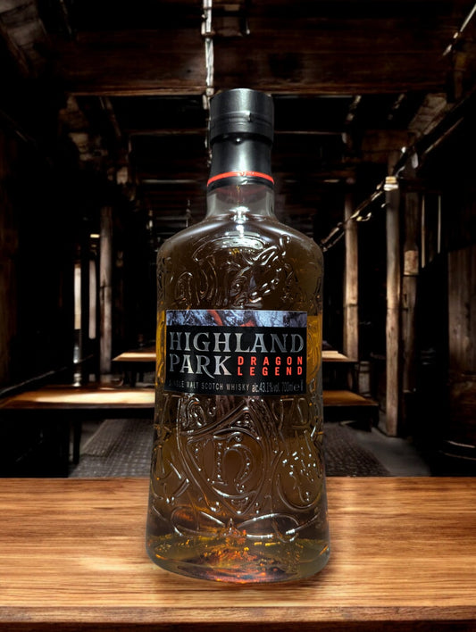 Eine Flasche Highland Park Dragon Legend Whisky in einer atmosphärischen Destilleriehalle, umgeben von rustikalem Holz und rauen Steinwänden. Die dunkle Flasche mit kunstvollem nordischen Drachen-Design sticht hervor und verleiht der Szenerie einen Hauch von mystischer Wikingertradition und handwerklicher Perfektion.