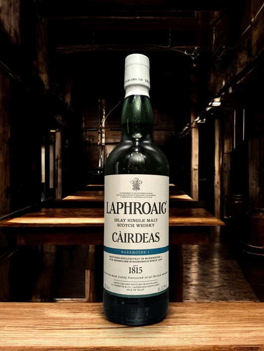 Flasche Laphroaig Cairdeas 2022 Warehouse 1 Edition Whisky mit markantem, dunklem Etikett und Siegel, präsentiert vor Fässern im Lagerhausstil, die die Herkunft und Exklusivität dieser limitierten Abfüllung betonen.