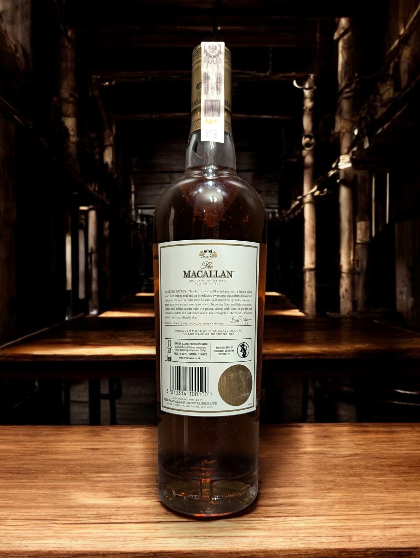 Flasche des Macallan Gold aus der 1824 Series, elegant dargestellt vor einem dunkelgrauen Hintergrund, mit einem sanft schimmernden, hellgoldenen Farbton des Whiskys, der durch das Glas leuchtet. Das Etikett reflektiert Luxus und Einfachheit, wodurch die Qualität und Reinheit dieser speziellen Abfüllung der Marke Macallan betont wird.