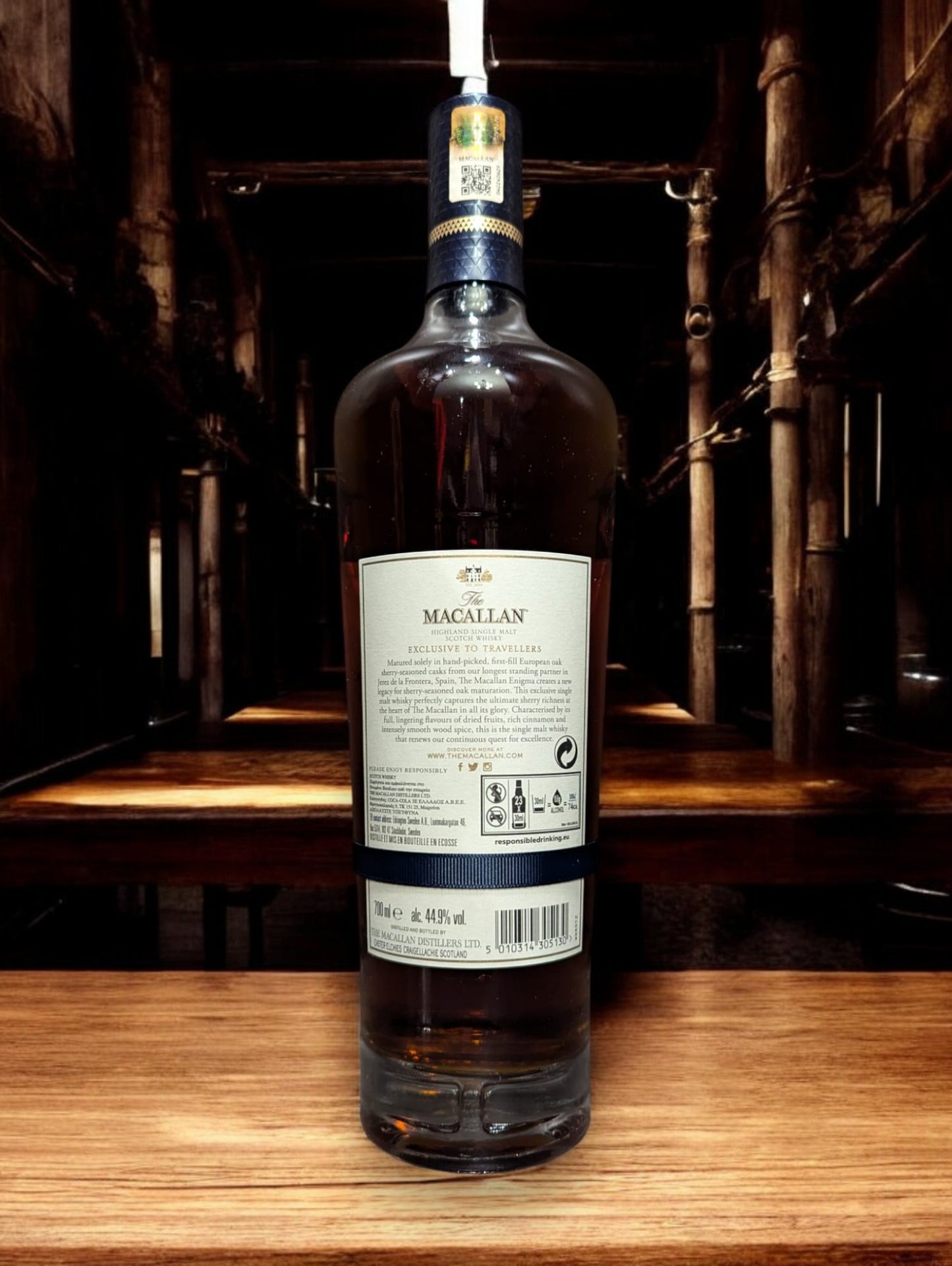 Flasche Macallan Enigma aus der Quest Collection, präsentiert vor einem dunkelgrauen Hintergrund, mit einem intensiven, rötlich-braunen Farbton des Whiskys, der durch das Glas schimmert, und einem auffälligen Etikett, das die Exklusivität und Rätselhaftigkeit dieser Abfüllung unterstreicht