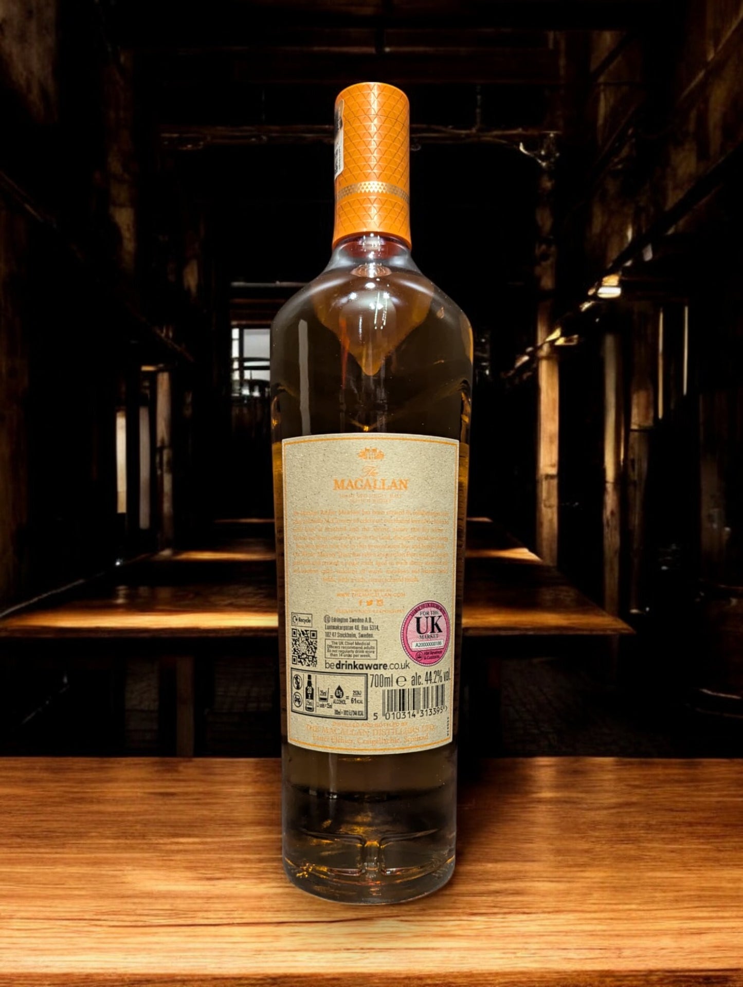 Flasche Macallan Harmony Collection Amber Meadow Whisky, elegant platziert vor einem dunkelgrauen Hintergrund, mit einem sanften Licht, das die reiche, honiggoldene Farbe des Whiskys und die raffinierten Details auf dem Etikett hervorhebt.