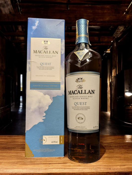 Flasche des Macallan Quest Single Malt Whisky aus der Quest Collection, positioniert vor einem dunkelgrauen Hintergrund, mit einem sanften, kupferfarbenen Schimmer des Whiskys und einem charakteristischen Etikett, das die Reise und das Abenteuer symbolisiert, welches diese Kollektion inspiriert hat.