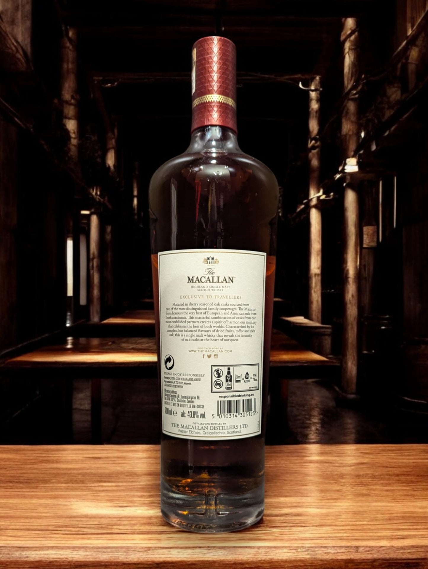 Flasche Macallan Terra aus der Quest Collection, elegant präsentiert vor einem dunkelgrauen Hintergrund. Der tiefe, bernsteinfarbene Whisky strahlt warm durch das Glas, während das luxuriöse Etikett in Erdtönen mit goldenen Akzenten die Verbindung zur Erde und den Reifeprozess in speziell ausgewählten Fässern repräsentiert.