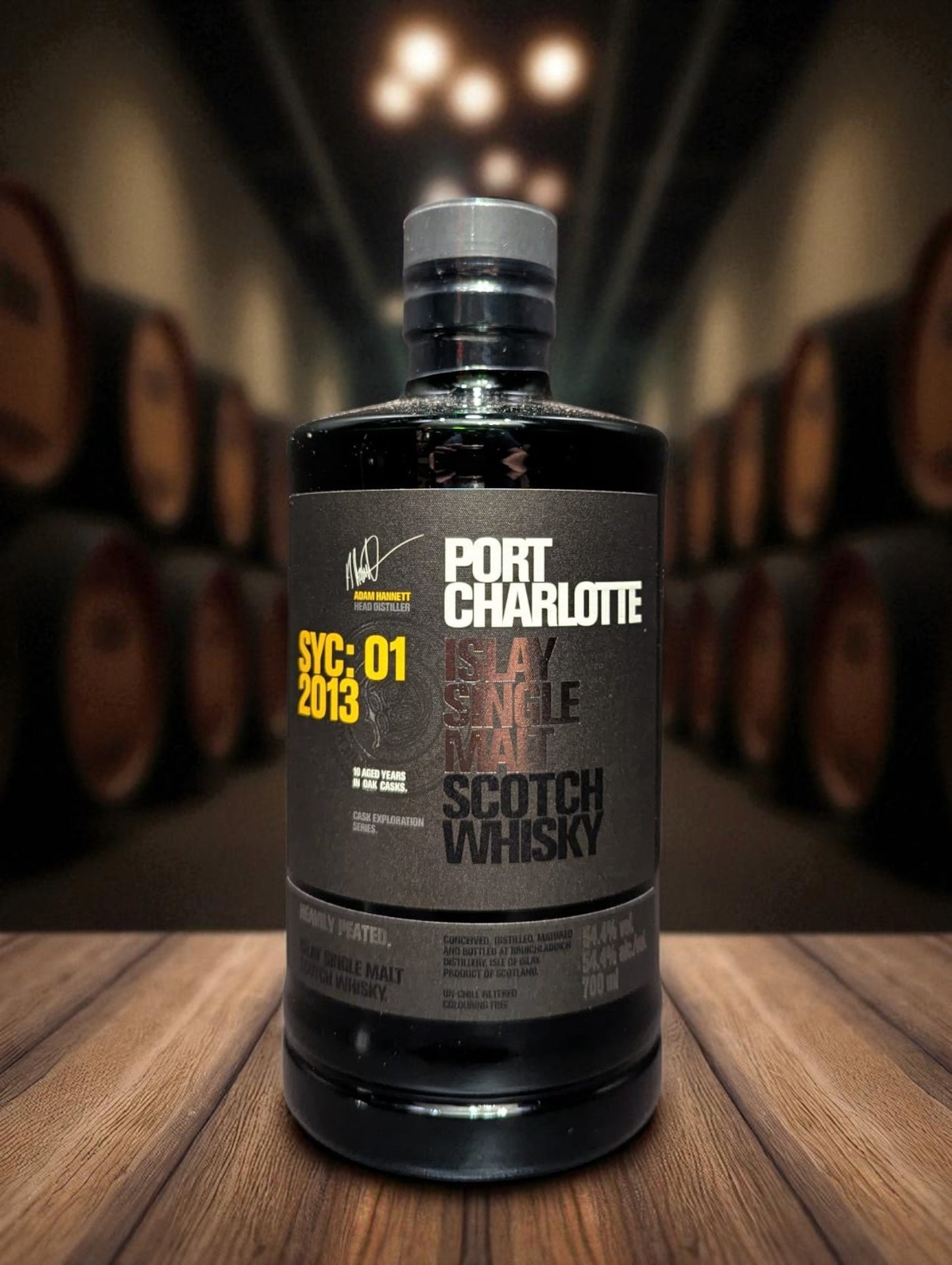 Eine Flasche Port Charlotte Whisky, vor dunklem Hintergrund mit Fässern