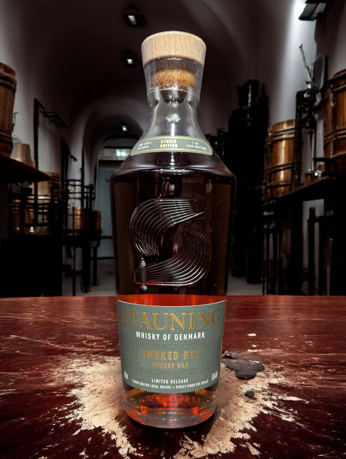 Stauning Smoked Rye - Danish Studio Edition Whisky auf einem Tisch vor dunklem Hintergrund einer Distille