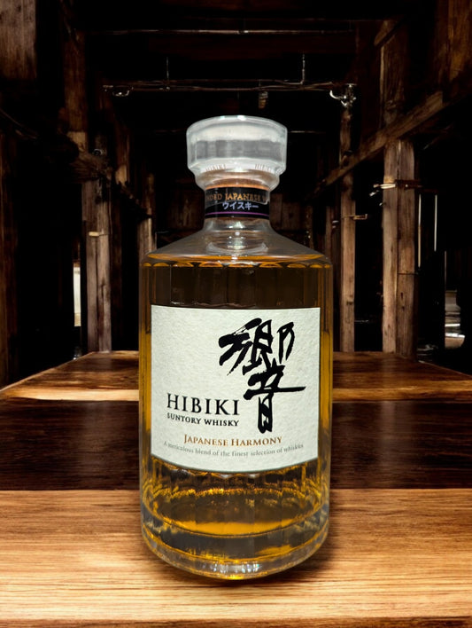 Flasche Suntory Hibiki Harmony Whisky vor einem dunkelgrauen Hintergrund, wobei das edle Design der Flasche mit ihrer facettenreichen Glasstruktur und das elegante Etikett mit goldener Schrift durch den Kontrast hervorgehoben werden und der goldene Farbton des Whiskys sanft durchscheint.