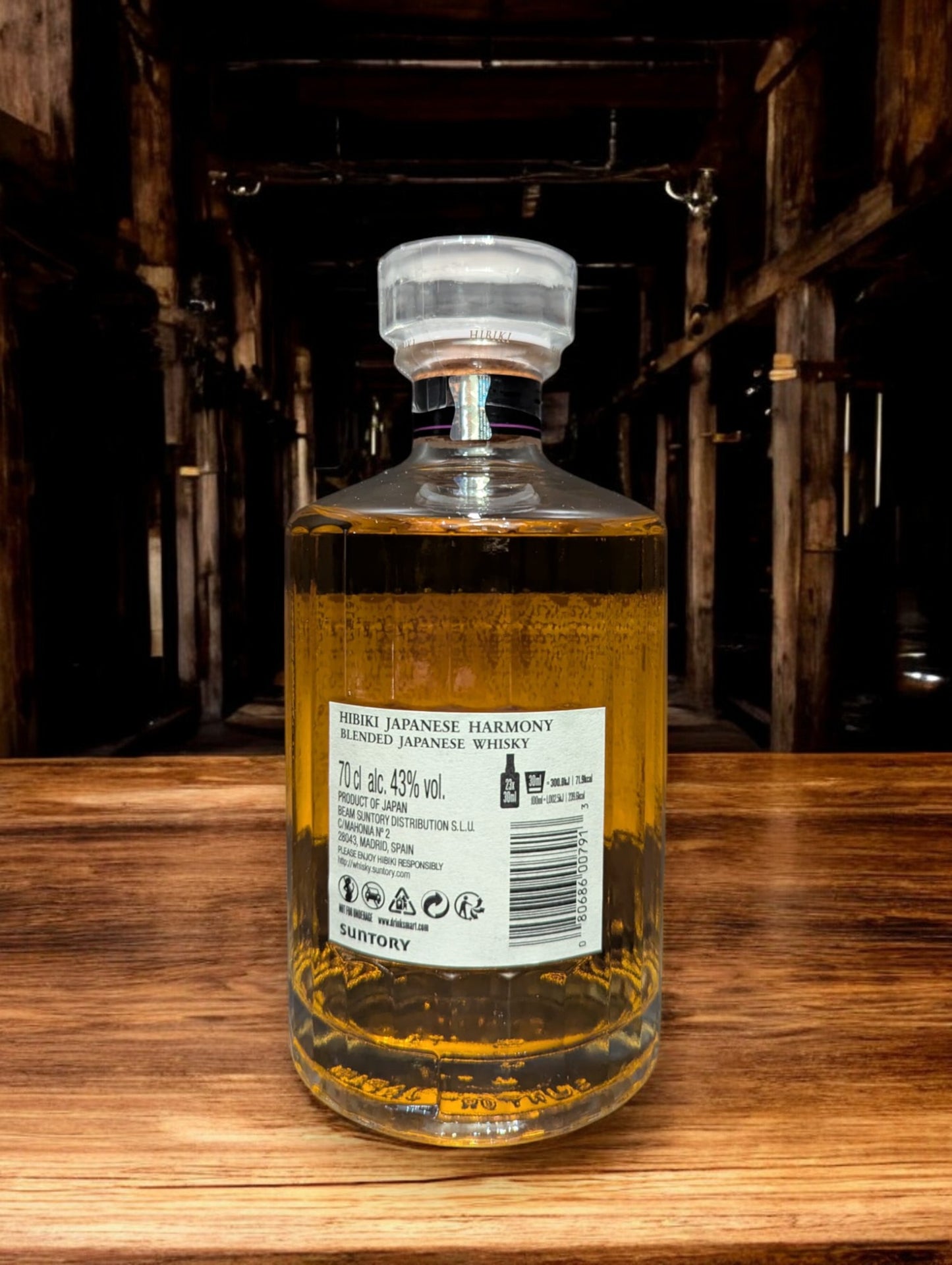 Flasche Suntory Hibiki Harmony Whisky vor einem dunkelgrauen Hintergrund, wobei das edle Design der Flasche mit ihrer facettenreichen Glasstruktur und das elegante Etikett mit goldener Schrift durch den Kontrast hervorgehoben werden und der goldene Farbton des Whiskys sanft durchscheint.