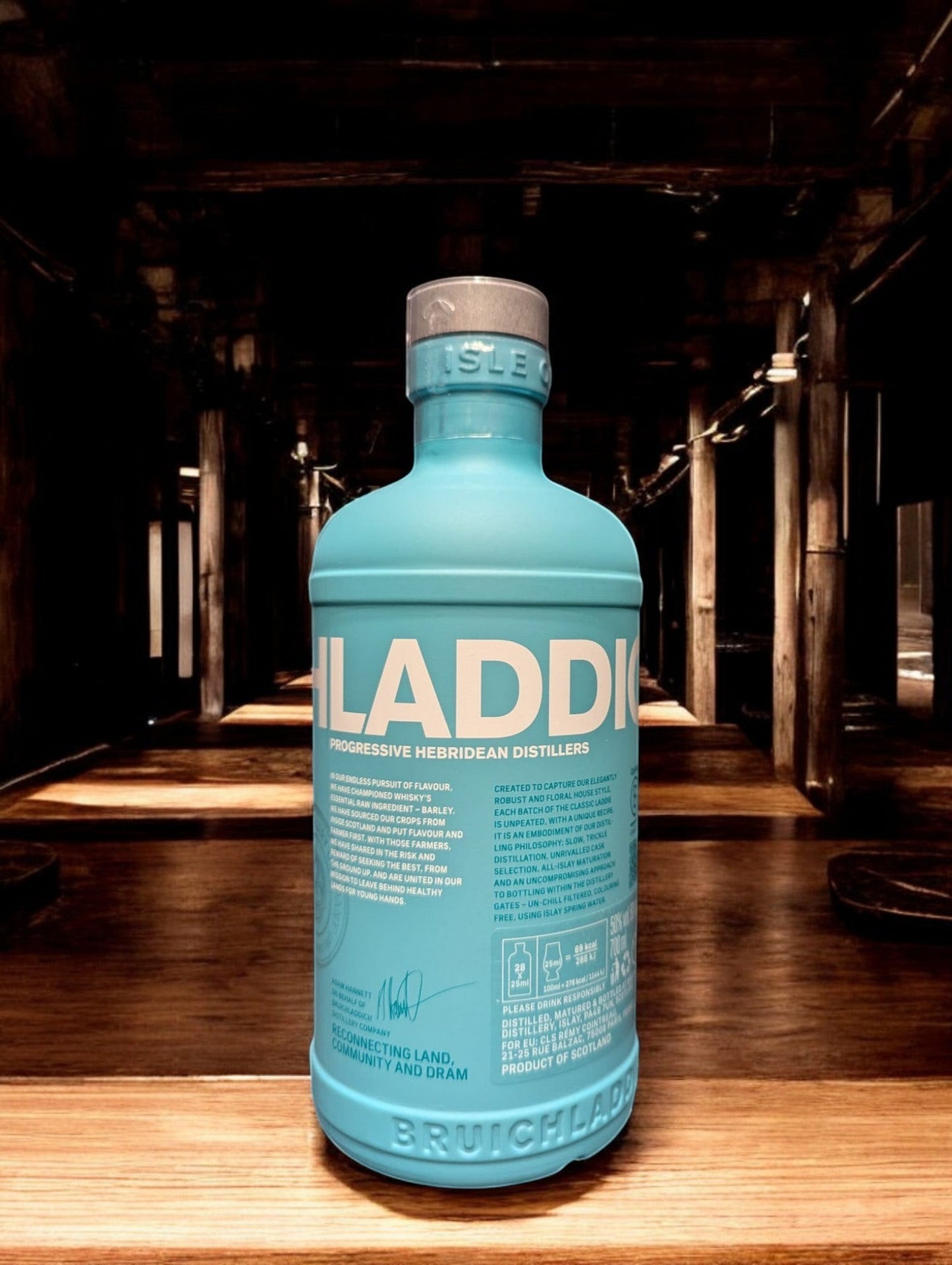 Ein Bruichladdich Classic Laddie Whisky in einer Destilleriehalle, umgeben von warmen Holzelementen, Kupferbrennblasen und Holzfässern. Die markante türkisfarbene Flasche hebt sich von der rustikalen Umgebung ab, die eine gemütliche und traditionelle Atmosphäre ausstrahlt.