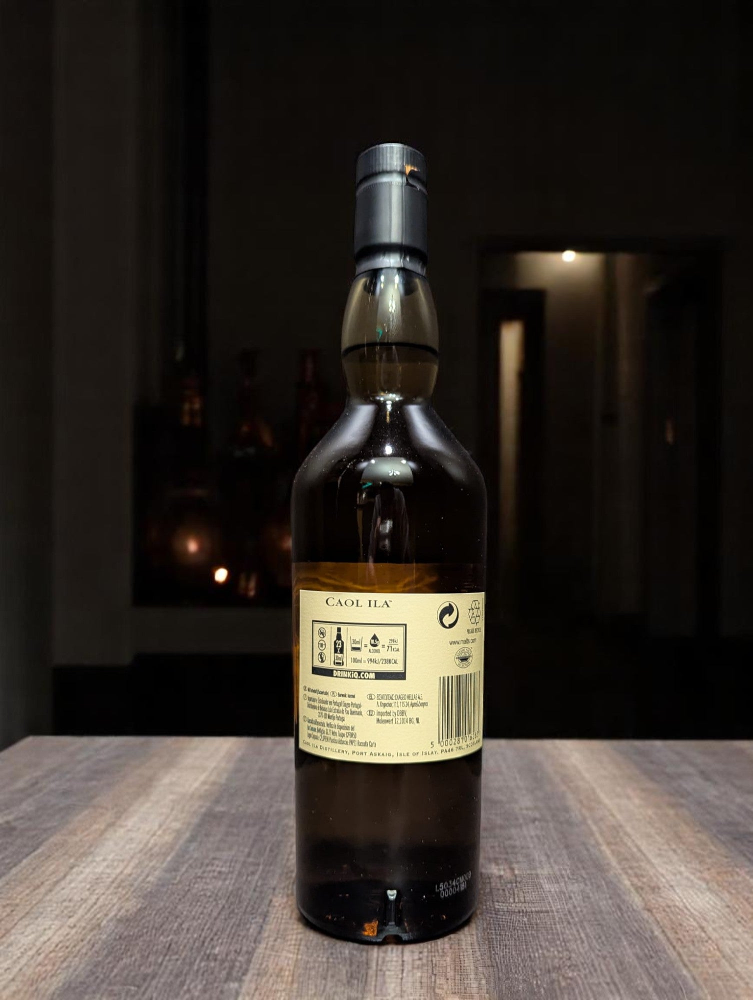 Flasche Caol Ila 12 Years Single Malt Whisky vor dunkler Destillerie-Kulisse.