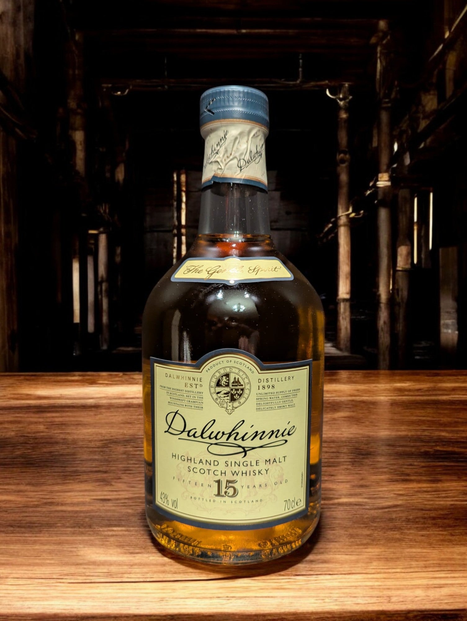 Eine Flasche Dalwhinnie 15 Jahre Single Malt Scotch Whisky steht aufrecht vor einem dunkelgrauen Hintergrund. Die elegante, klare Glasflasche zeigt ein cremefarbenes Etikett mit goldenen Akzenten und schwarzer Schrift. Der goldene Whisky schimmert im Licht und wird von einem markanten, kugelförmigen Flaschenhals mit einem schwarzen Verschluss gekrönt. Die gesamte Szene wirkt edel und zeitlos, was die hohe Qualität des Whiskys unterstreicht.