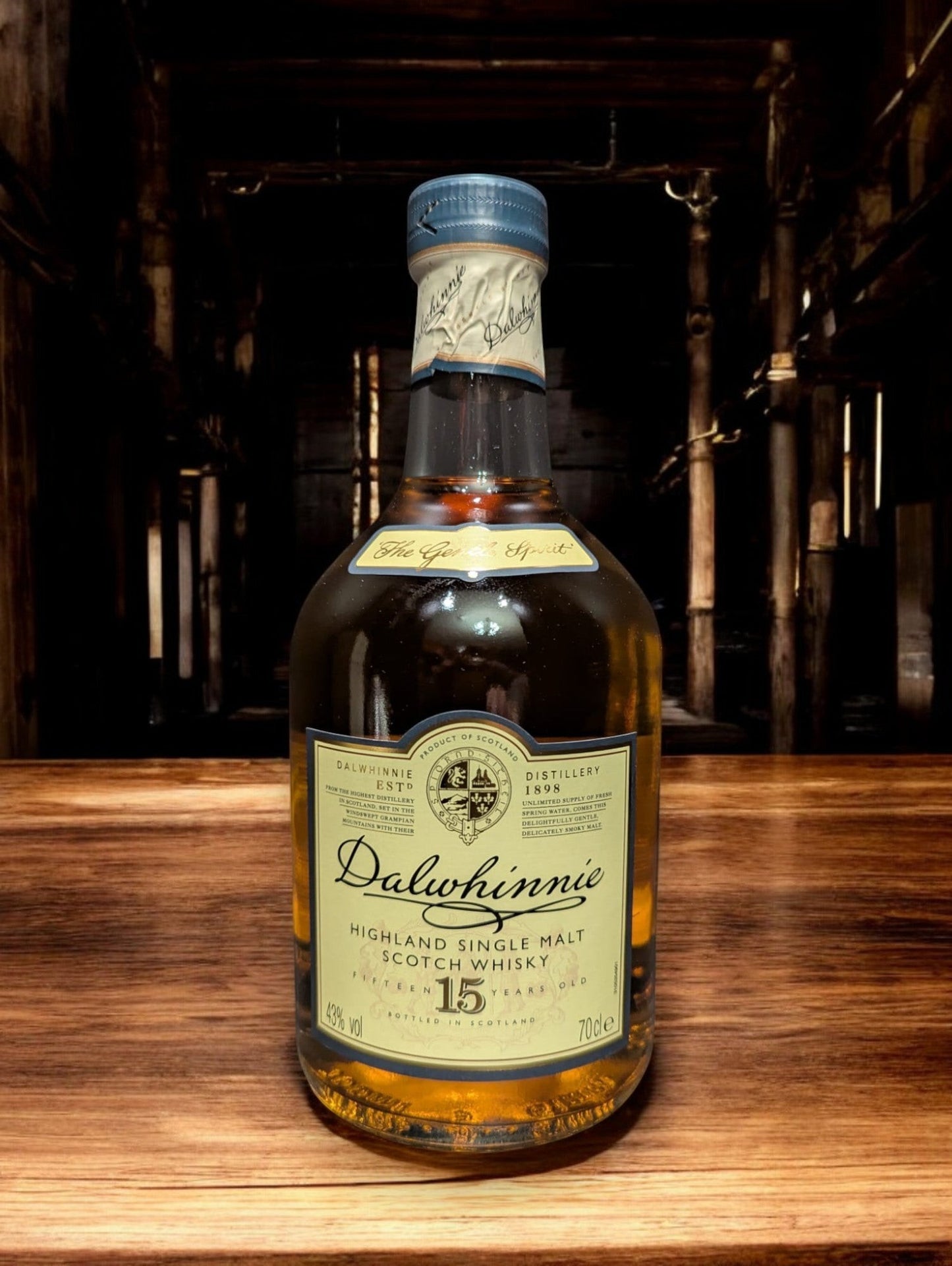 Eine Flasche Dalwhinnie 15 Jahre Single Malt Scotch Whisky steht aufrecht vor einem dunkelgrauen Hintergrund. Die elegante, klare Glasflasche zeigt ein cremefarbenes Etikett mit goldenen Akzenten und schwarzer Schrift. Der goldene Whisky schimmert im Licht und wird von einem markanten, kugelförmigen Flaschenhals mit einem schwarzen Verschluss gekrönt. Die gesamte Szene wirkt edel und zeitlos, was die hohe Qualität des Whiskys unterstreicht.