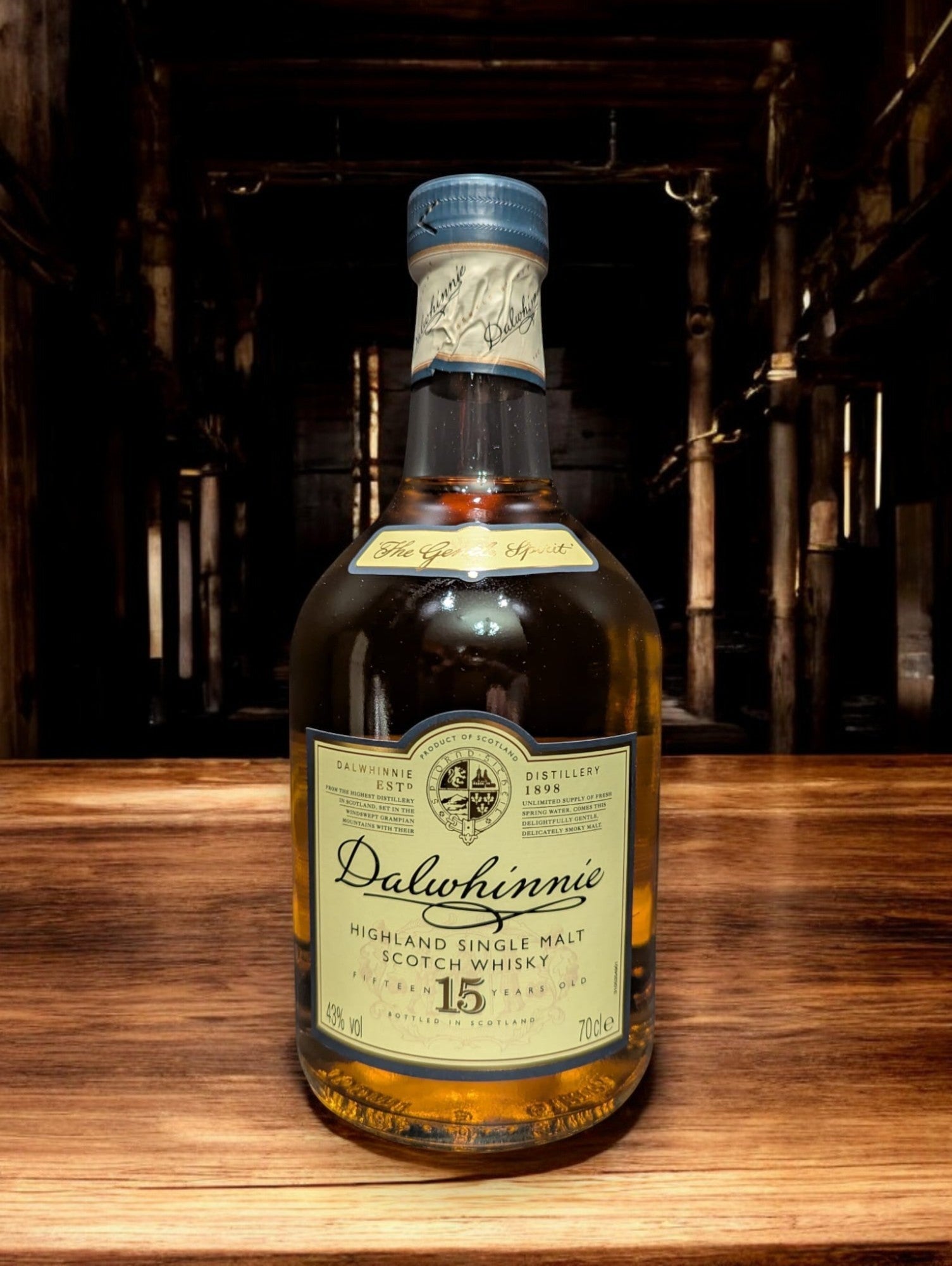 Eine Flasche Dalwhinnie 15 Jahre Single Malt Scotch Whisky steht aufrecht vor einem dunkelgrauen Hintergrund. Die elegante, klare Glasflasche zeigt ein cremefarbenes Etikett mit goldenen Akzenten und schwarzer Schrift. Der goldene Whisky schimmert im Licht und wird von einem markanten, kugelförmigen Flaschenhals mit einem schwarzen Verschluss gekrönt. Die gesamte Szene wirkt edel und zeitlos, was die hohe Qualität des Whiskys unterstreicht.