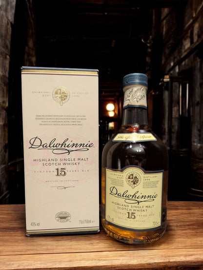 Eine Flasche Dalwhinnie 15 Jahre Single Malt Scotch Whisky steht aufrecht vor einem dunkelgrauen Hintergrund. Die elegante, klare Glasflasche zeigt ein cremefarbenes Etikett mit goldenen Akzenten und schwarzer Schrift. Der goldene Whisky schimmert im Licht und wird von einem markanten, kugelförmigen Flaschenhals mit einem schwarzen Verschluss gekrönt. Die gesamte Szene wirkt edel und zeitlos, was die hohe Qualität des Whiskys unterstreicht.