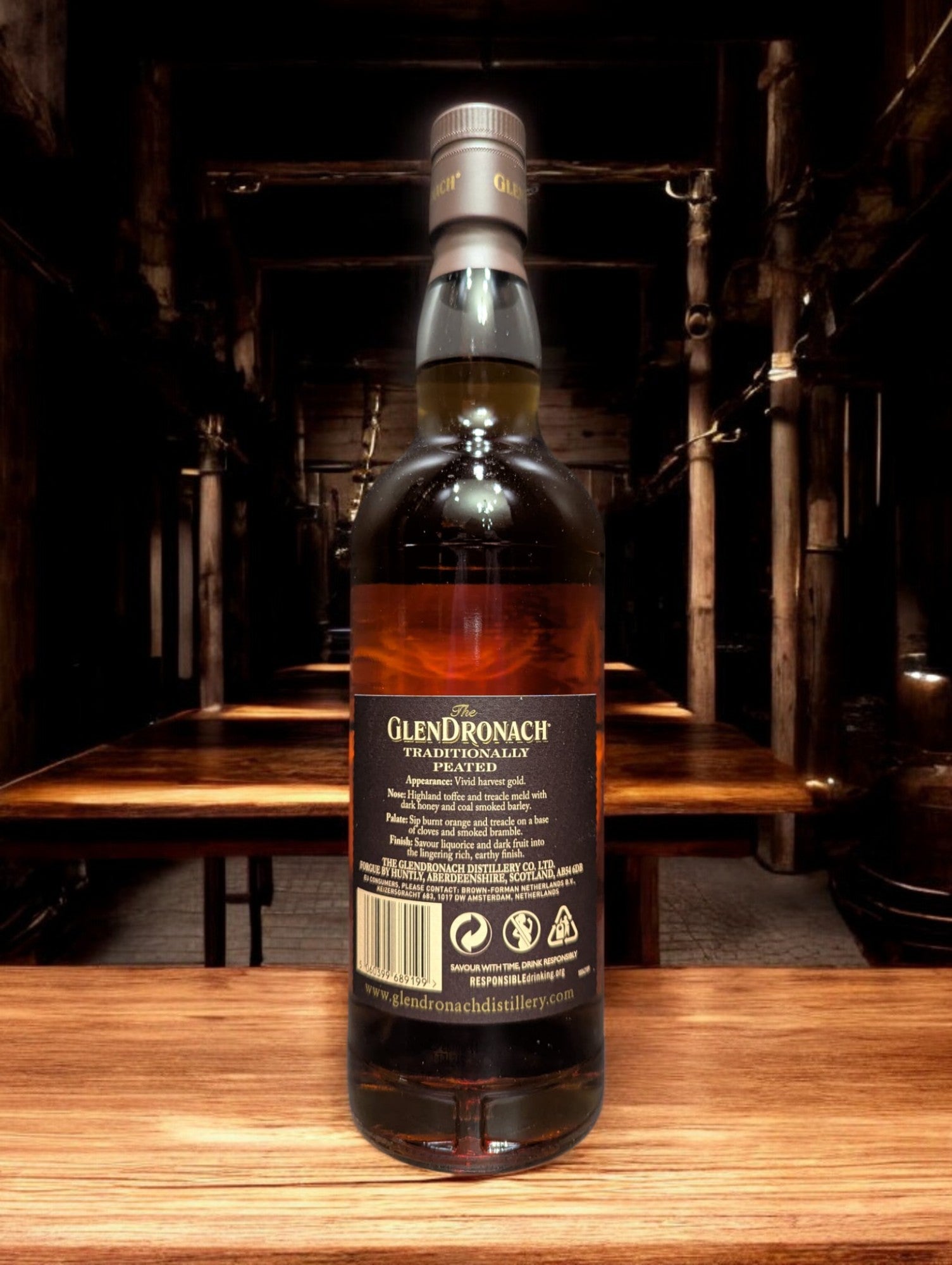 Eine Flasche Glendronach Traditionally Peated Whisky in einer stimmungsvollen Destilleriehalle, umgeben von massiven Holzfässern und alten Steinmauern. Die dunkle, edle Flasche mit goldenen Akzenten steht im Kontrast zur rustikalen Umgebung und vermittelt einen Hauch von traditionellem Handwerk und Whiskygeschichte.
