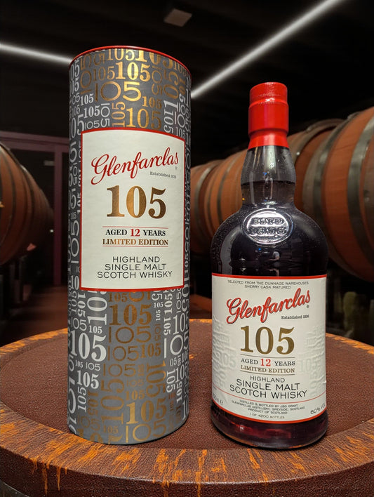 Glenfarclas 105 Hourglass Limited Edition Whisky bottle on weathered dark brown wooden table in traditional distillery setting with copper stills and oak barrels in shadowy background