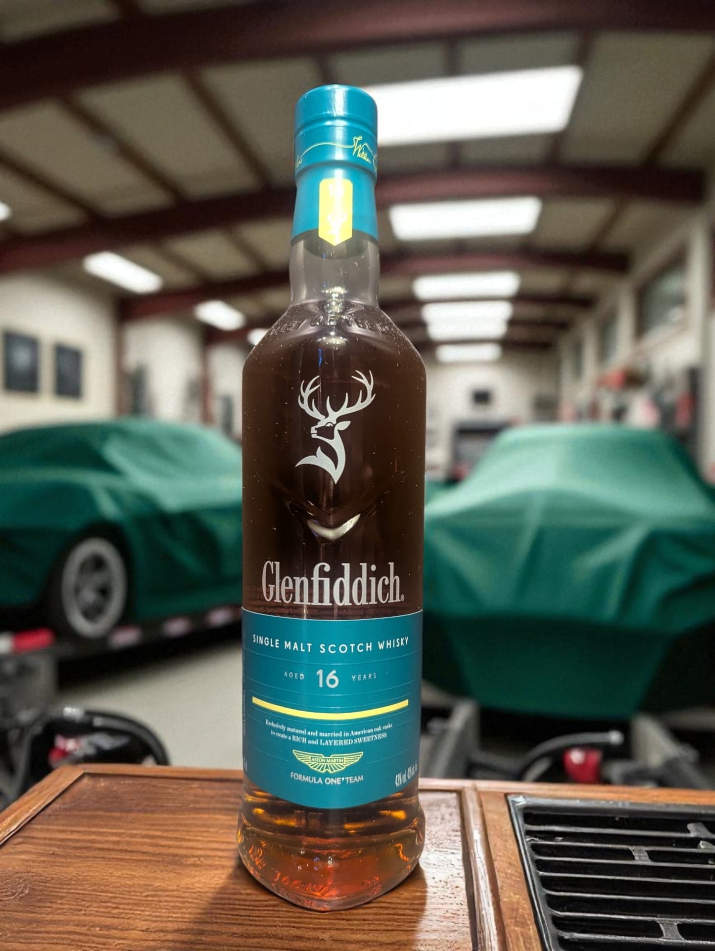 Flasche und Verpackung Glenfiddich 16 in einer Garage vor abgedecktem Aston Martin
