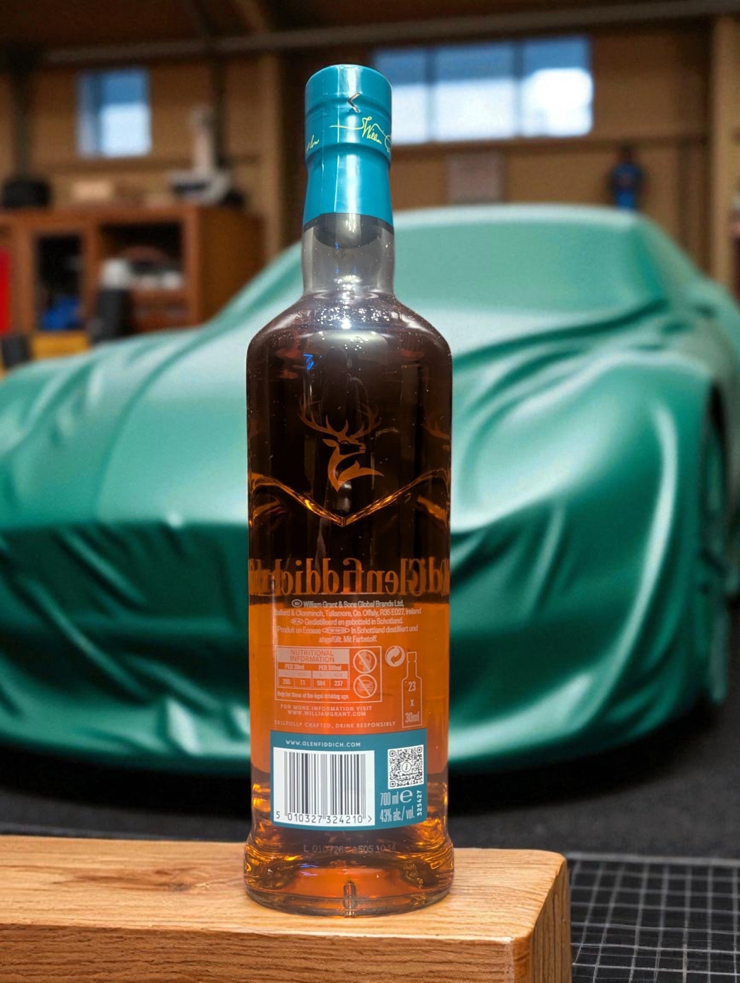 Flasche und Verpackung Glenfiddich 16 in einer Garage vor abgedecktem Aston Martin