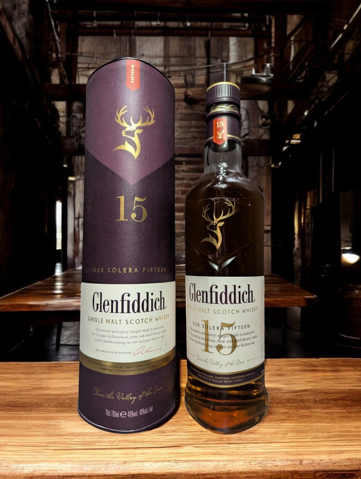 Ein Glenfiddich 15 Jahre Whisky in einer eleganten Flasche, umgeben von einer stilvollen Verpackung. Die goldene Farbe des Whiskys wird durch das Licht betont, während das Etikett die reiche Tradition und Qualität der Marke hervorhebt. Ideal präsentiert auf einem dunklen Holztisch mit einem passenden Whiskyglas, das einen Hauch von Luxus vermittelt.