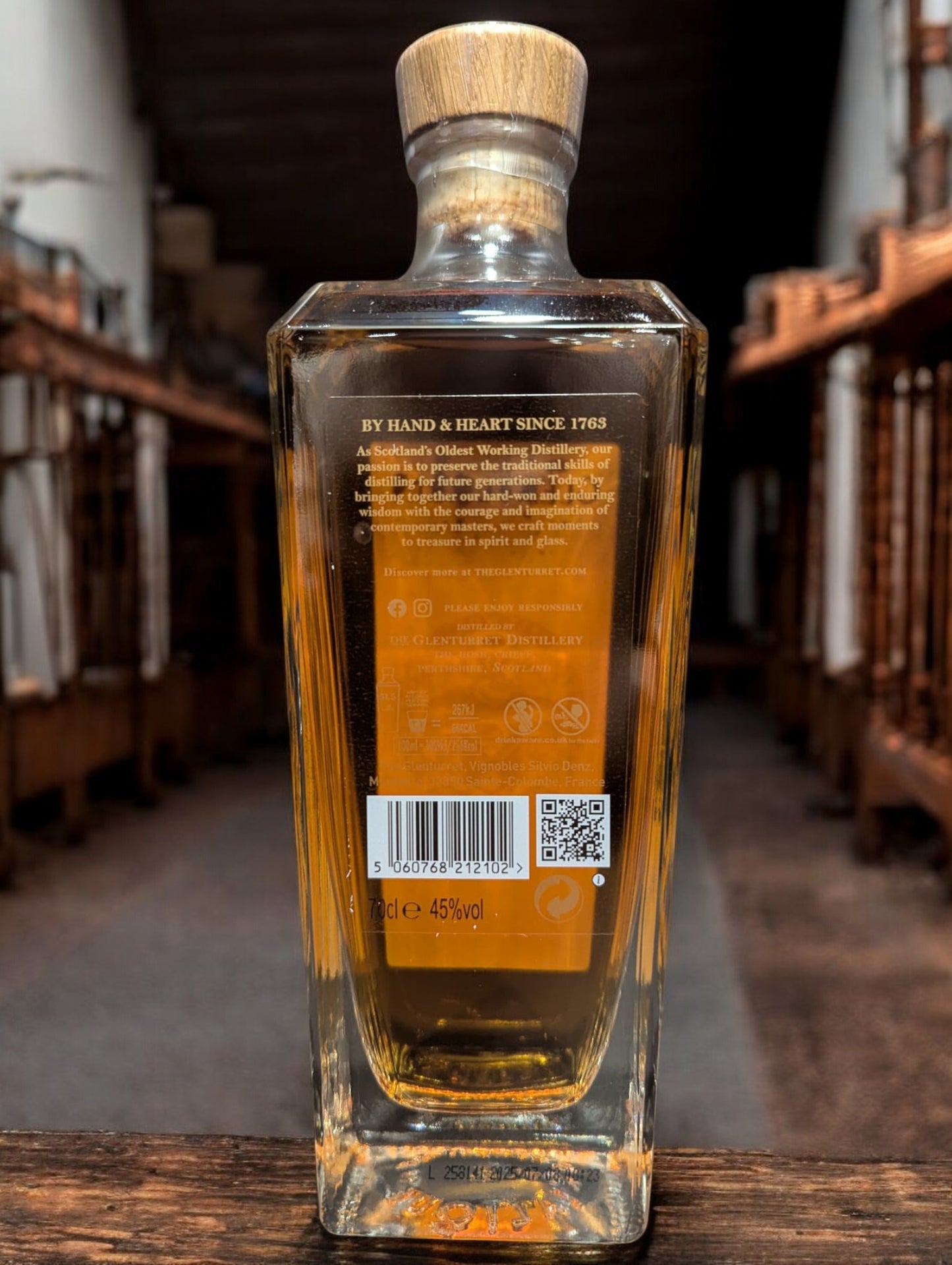 Eine Flasche Glenturret Triple Wood 2025 Whisky vor dunklem Distillenhintergrund