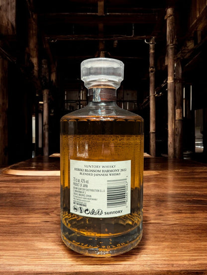 Flasche von Hibiki Blossom Harmony Whisky, umgeben von zarten Kirschblüten, auf einem eleganten dunklen Hintergrund, der die warmen Bernsteintöne des Getränks hervorhebt.