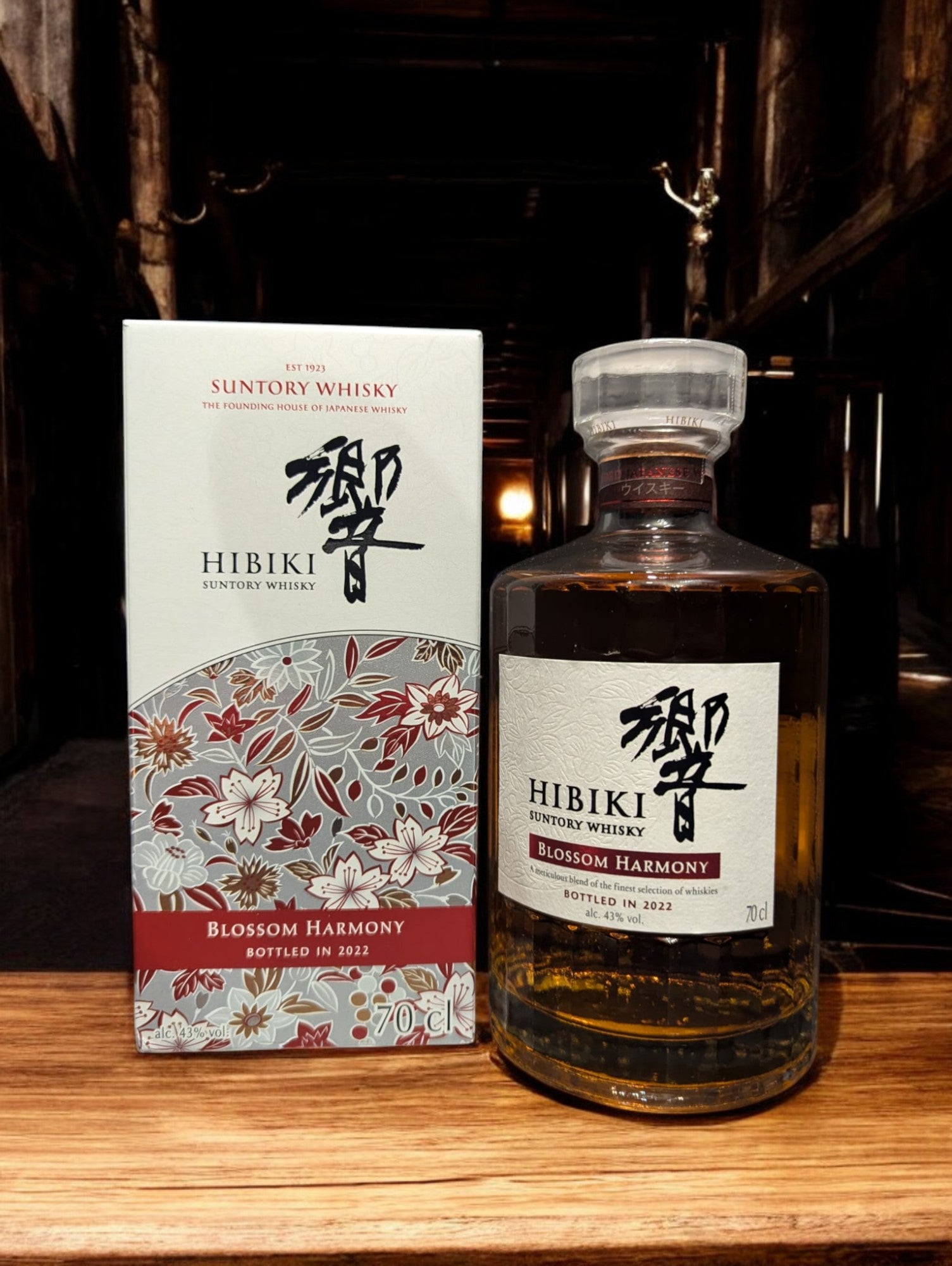 Flasche von Hibiki Blossom Harmony Whisky, umgeben von zarten Kirschblüten, auf einem eleganten dunklen Hintergrund, der die warmen Bernsteintöne des Getränks hervorhebt.