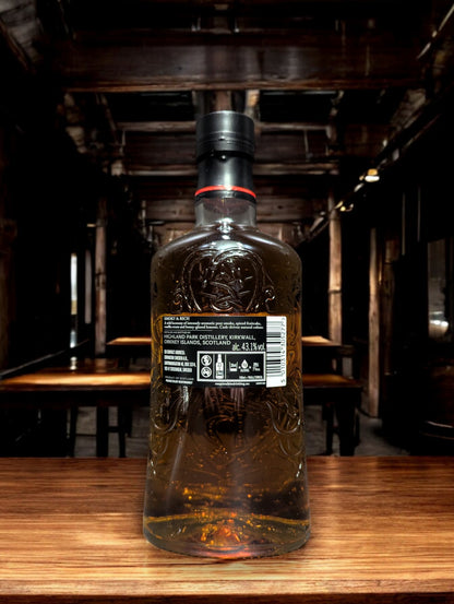 Eine Flasche Highland Park Dragon Legend Whisky in einer atmosphärischen Destilleriehalle, umgeben von rustikalem Holz und rauen Steinwänden. Die dunkle Flasche mit kunstvollem nordischen Drachen-Design sticht hervor und verleiht der Szenerie einen Hauch von mystischer Wikingertradition und handwerklicher Perfektion.