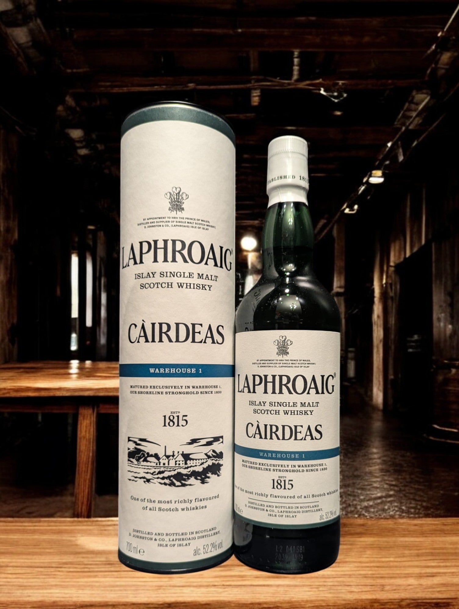 Flasche Laphroaig Cairdeas 2022 Warehouse 1 Edition Whisky mit markantem, dunklem Etikett und Siegel, präsentiert vor Fässern im Lagerhausstil, die die Herkunft und Exklusivität dieser limitierten Abfüllung betonen.