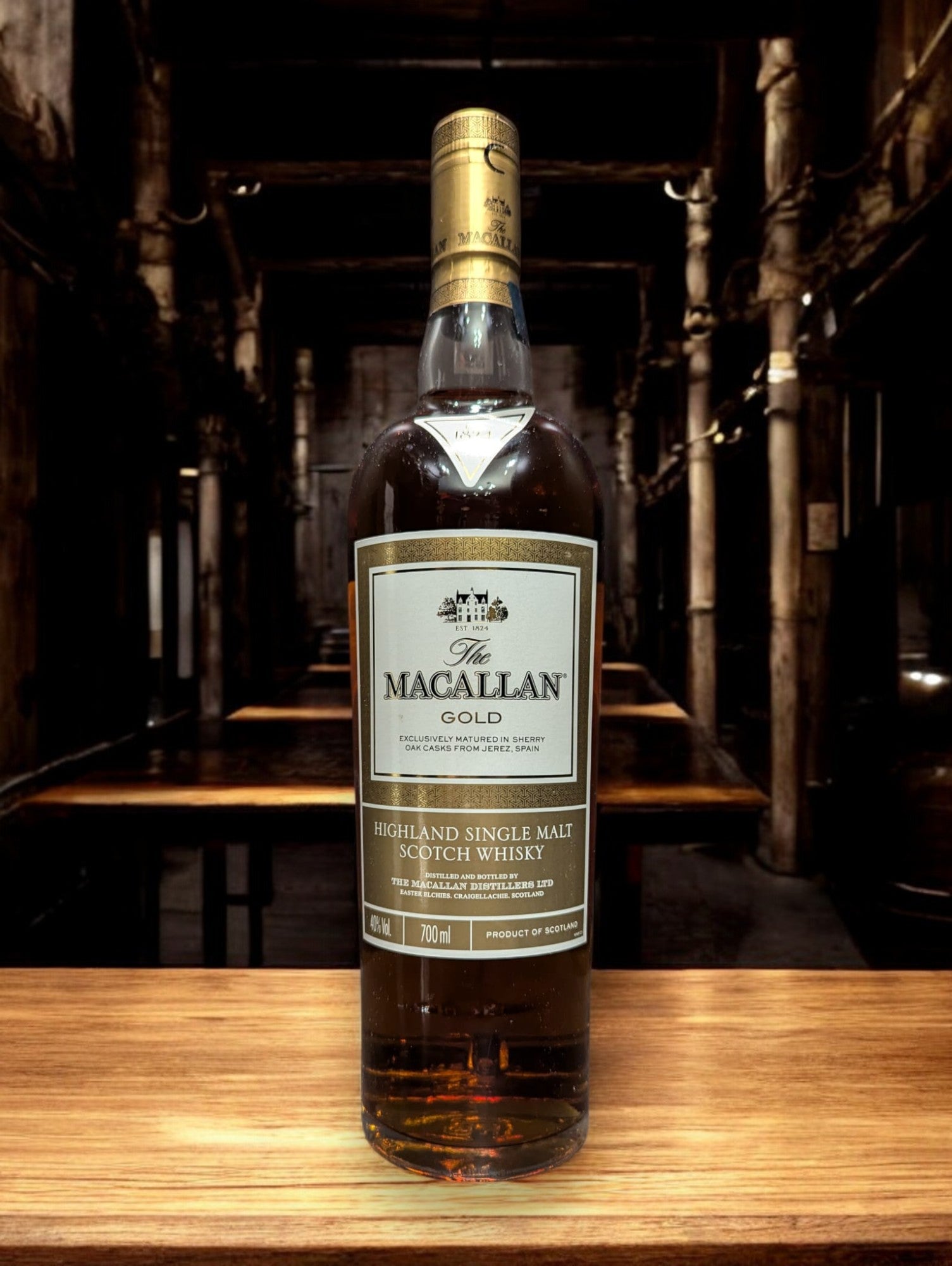 Flasche des Macallan Gold aus der 1824 Series, elegant dargestellt vor einem dunkelgrauen Hintergrund, mit einem sanft schimmernden, hellgoldenen Farbton des Whiskys, der durch das Glas leuchtet. Das Etikett reflektiert Luxus und Einfachheit, wodurch die Qualität und Reinheit dieser speziellen Abfüllung der Marke Macallan betont wird.