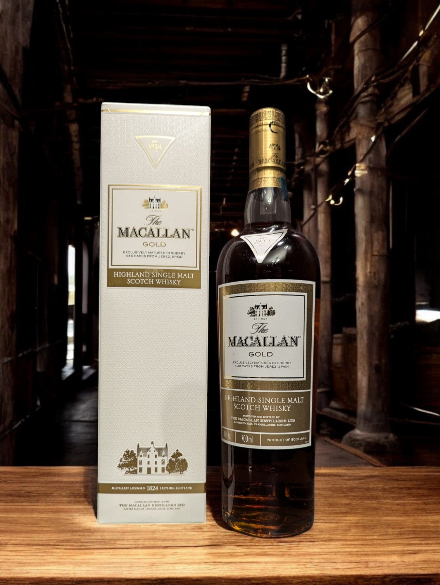 Flasche des Macallan Gold aus der 1824 Series, elegant dargestellt vor einem dunkelgrauen Hintergrund, mit einem sanft schimmernden, hellgoldenen Farbton des Whiskys, der durch das Glas leuchtet. Das Etikett reflektiert Luxus und Einfachheit, wodurch die Qualität und Reinheit dieser speziellen Abfüllung der Marke Macallan betont wird.