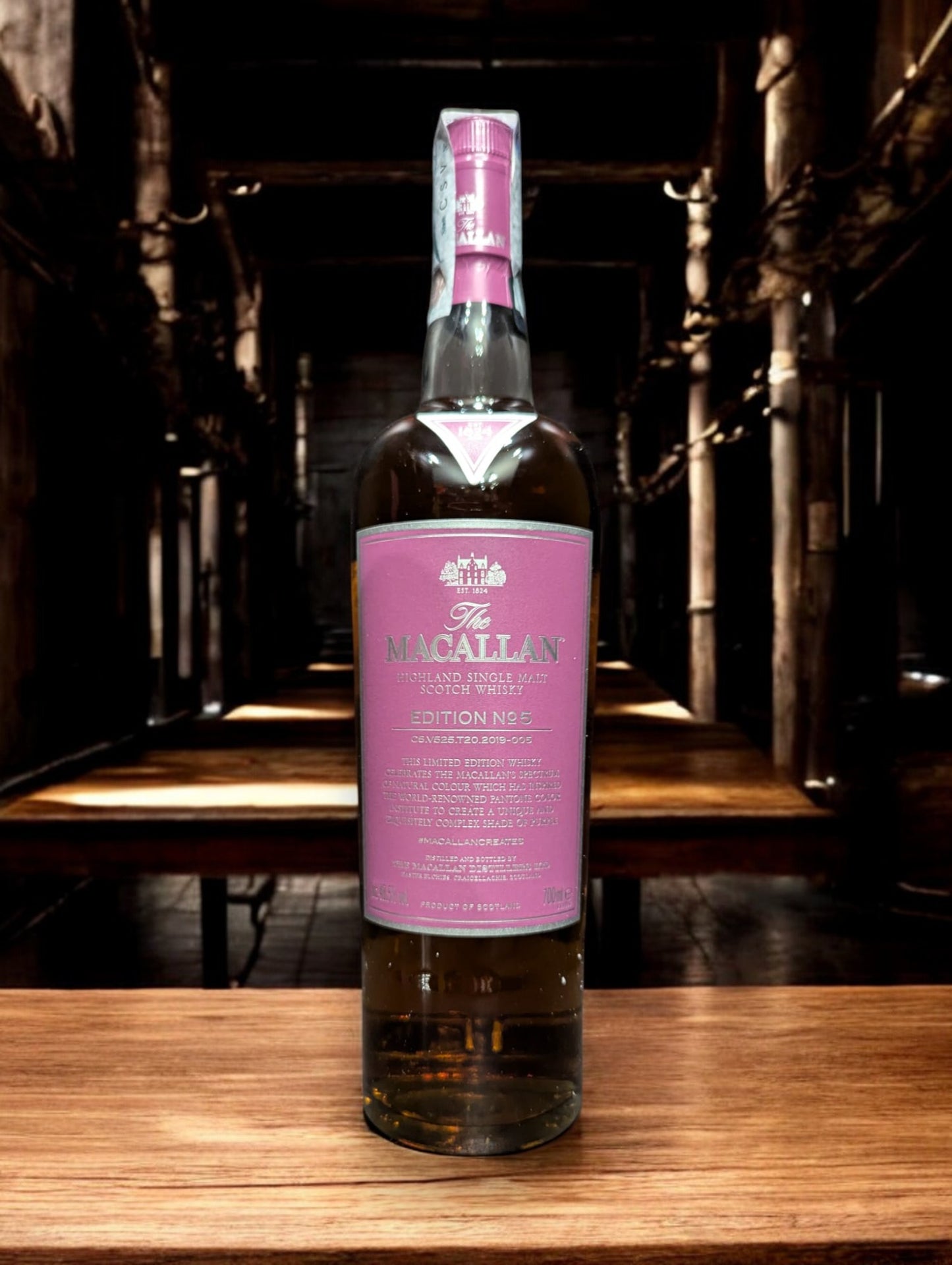 Eine Flasche von The Macallan Edition No. 5, kunstvoll inszeniert gegen einen einfachen Hintergrund, um die Bedeutung der natürlichen Farbe des Whiskys zu betonen. Das lebendige, lila Etikett und die Verpackung feiern die Farbpalette, die in der Whiskyherstellung ohne zusätzliche Farbstoffe entsteht, und ehren so die Reinheit und Ästhetik des Destillats.