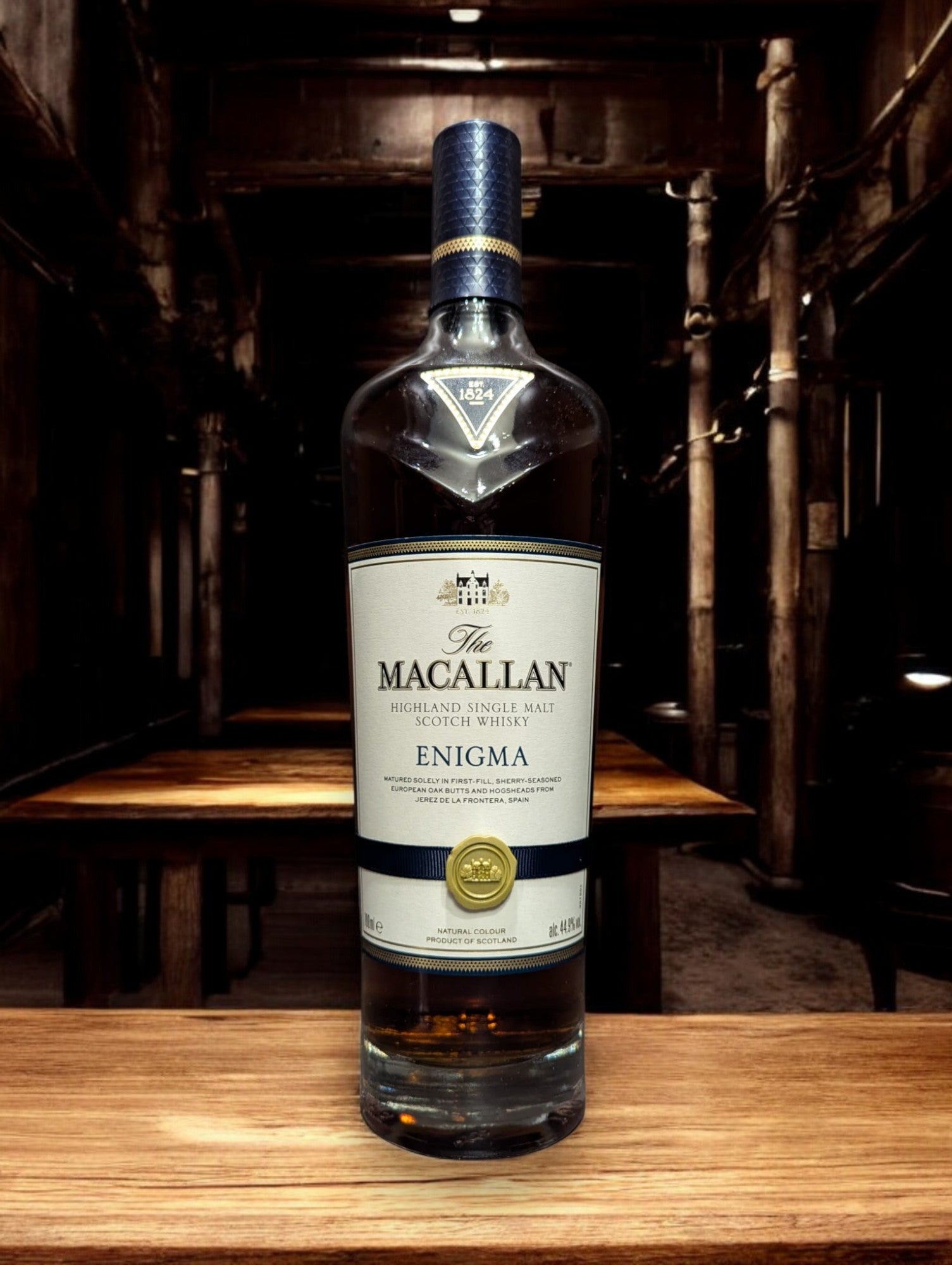 Flasche Macallan Enigma aus der Quest Collection, präsentiert vor einem dunkelgrauen Hintergrund, mit einem intensiven, rötlich-braunen Farbton des Whiskys, der durch das Glas schimmert, und einem auffälligen Etikett, das die Exklusivität und Rätselhaftigkeit dieser Abfüllung unterstreicht