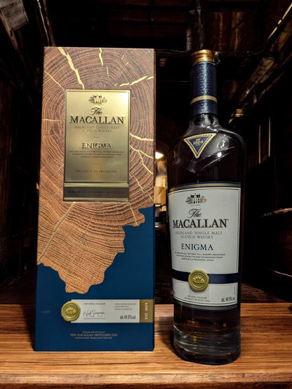 Flasche Macallan Enigma aus der Quest Collection, präsentiert vor einem dunkelgrauen Hintergrund, mit einem intensiven, rötlich-braunen Farbton des Whiskys, der durch das Glas schimmert, und einem auffälligen Etikett, das die Exklusivität und Rätselhaftigkeit dieser Abfüllung unterstreicht