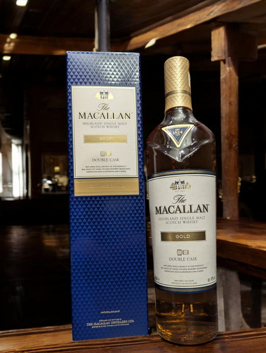 Flasche Macallan Gold Whisky präsentiert sich vor einem dunkelgrauen Hintergrund, wobei das warme, bernsteinfarbene Leuchten des Whiskys und das markante Etikett im Fokus stehen.