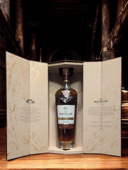 Exquisite Flasche Macallan Rare Cask 2022, sorgfältig platziert vor einem dunkelgrauen Hintergrund, was die reiche, rubinrote Farbe des Whiskys hervorhebt. Die Flasche zeichnet sich durch ihr luxuriöses Design aus, mit einem auffälligen, schwarz-goldenen Etikett, das die Seltenheit und Exklusivität dieses herausragenden Jahrgangs unterstreicht.
