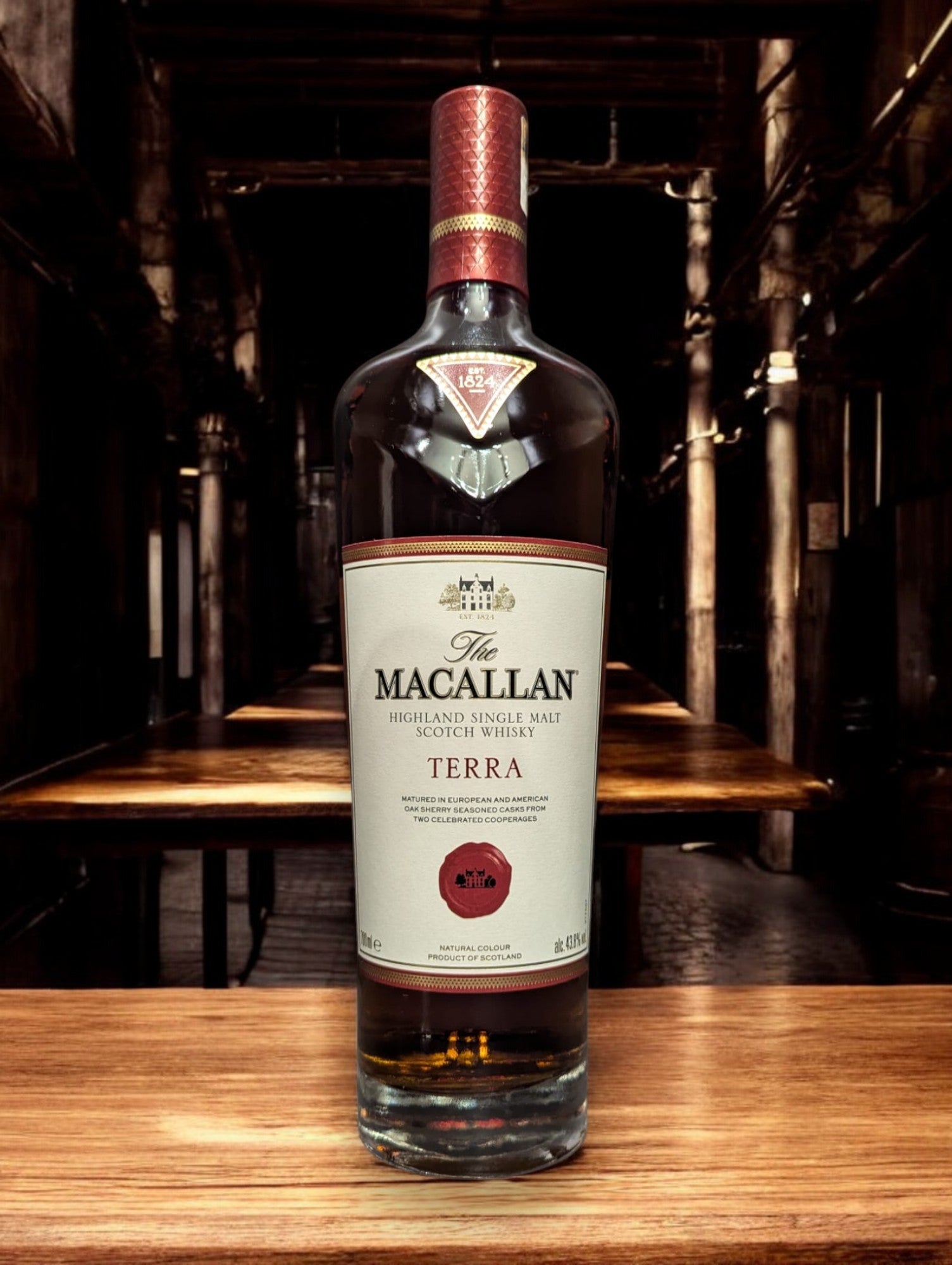 Flasche Macallan Terra aus der Quest Collection, elegant präsentiert vor einem dunkelgrauen Hintergrund. Der tiefe, bernsteinfarbene Whisky strahlt warm durch das Glas, während das luxuriöse Etikett in Erdtönen mit goldenen Akzenten die Verbindung zur Erde und den Reifeprozess in speziell ausgewählten Fässern repräsentiert.