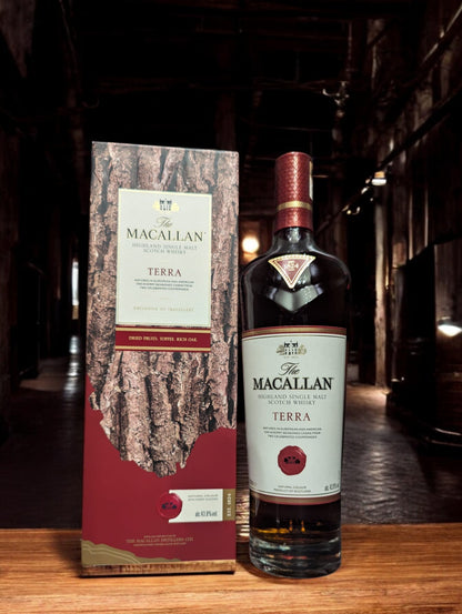 Flasche Macallan Terra aus der Quest Collection, elegant präsentiert vor einem dunkelgrauen Hintergrund. Der tiefe, bernsteinfarbene Whisky strahlt warm durch das Glas, während das luxuriöse Etikett in Erdtönen mit goldenen Akzenten die Verbindung zur Erde und den Reifeprozess in speziell ausgewählten Fässern repräsentiert.