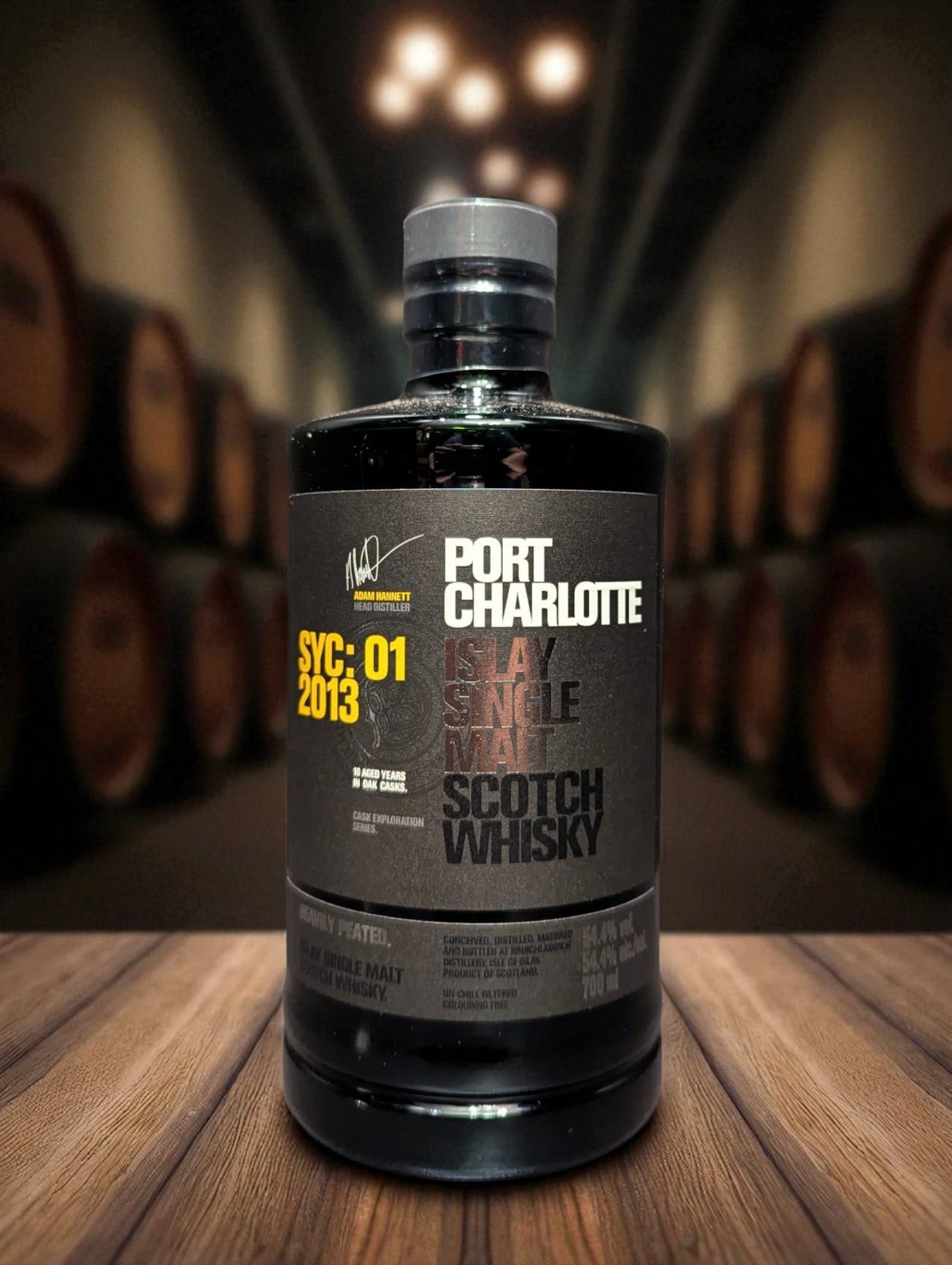 Eine Flasche Port Charlotte Whisky, vor dunklem Hintergrund mit Fässern