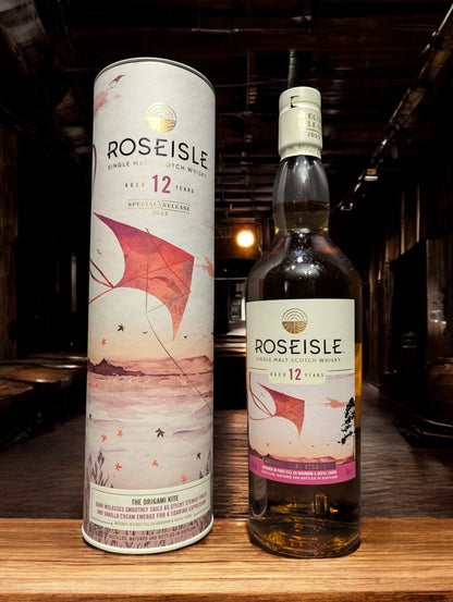 Flasche Roseisle 12 Jahre Single Malt Whisky steht im Vordergrund, scharf fokussiert, mit einem unscharfen industriellen Hintergrund aus Edelstahltanks und Rohrleitungen, die an einen modernen Brennereibetrieb erinnern.