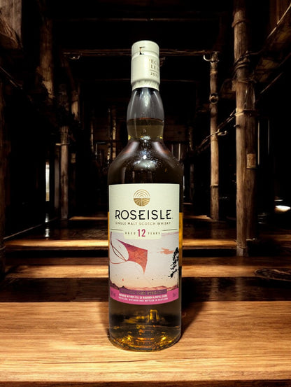 Flasche Roseisle 12 Jahre Single Malt Whisky steht im Vordergrund, scharf fokussiert, mit einem unscharfen industriellen Hintergrund aus Edelstahltanks und Rohrleitungen, die an einen modernen Brennereibetrieb erinnern.