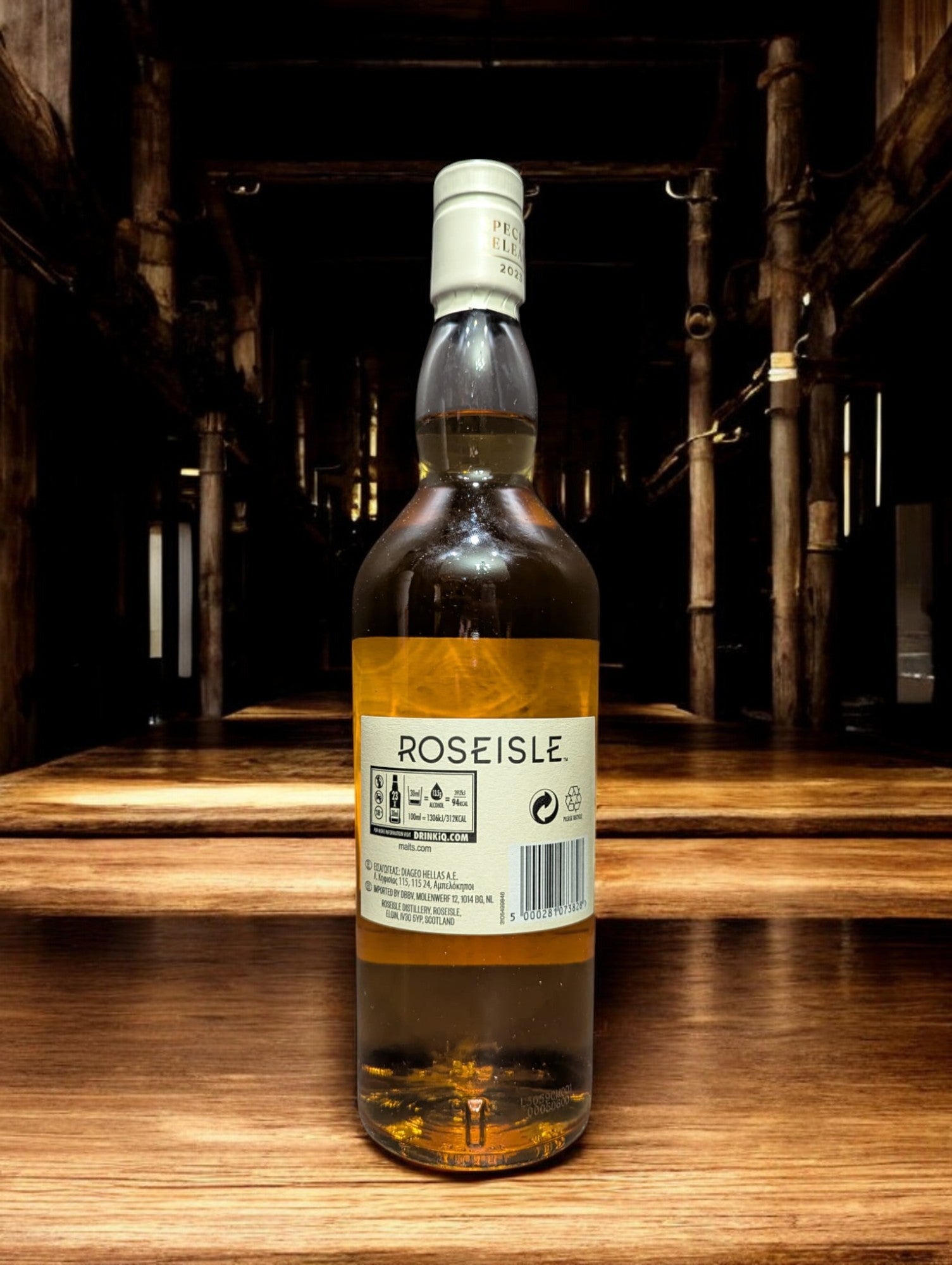 Flasche Roseisle 12 Jahre Single Malt Whisky steht im Vordergrund, scharf fokussiert, mit einem unscharfen industriellen Hintergrund aus Edelstahltanks und Rohrleitungen, die an einen modernen Brennereibetrieb erinnern.
